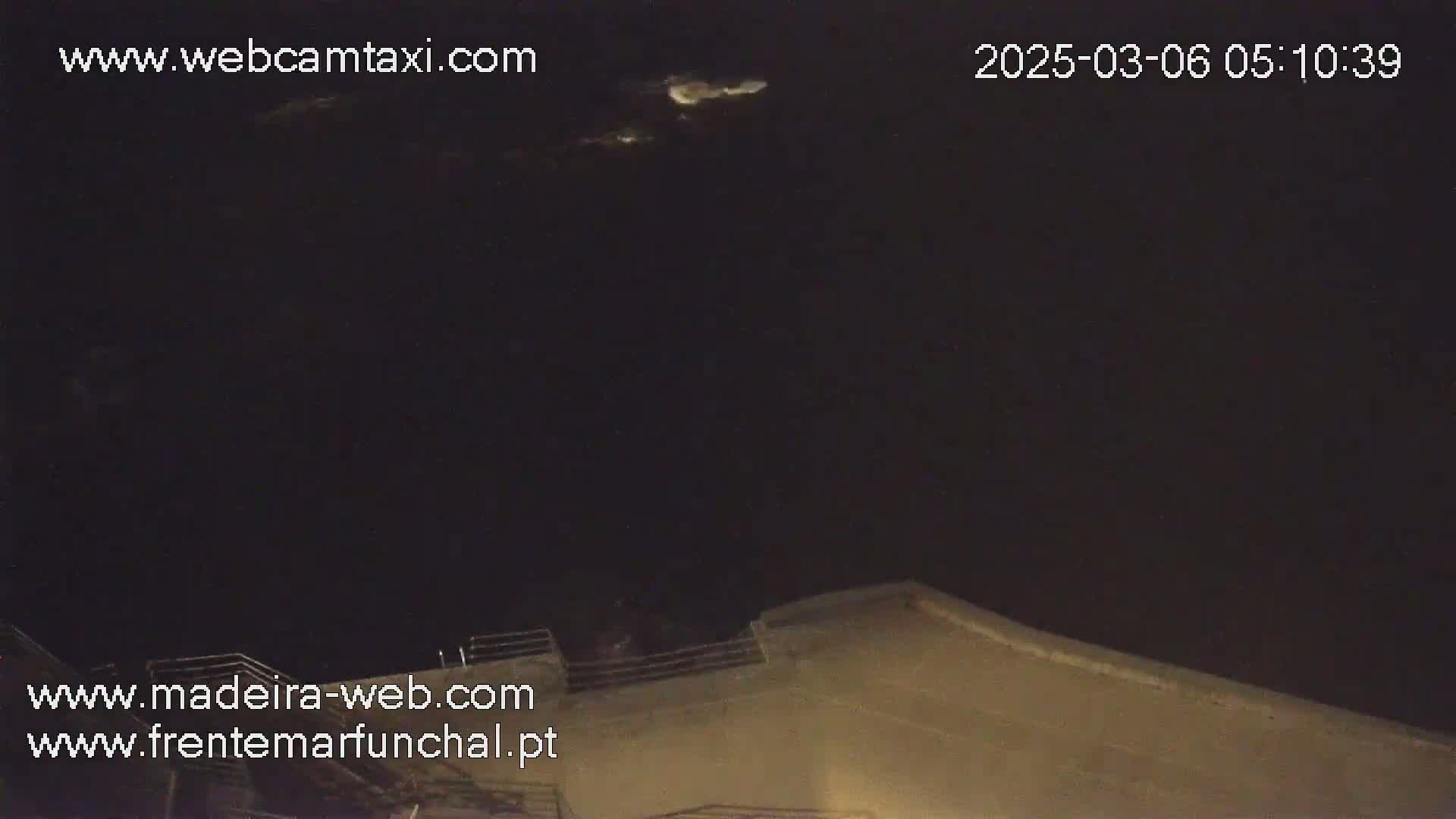 A nighttime, dark image shows a portion of a building's rooftop under a mostly clear sky with a few faint clouds.