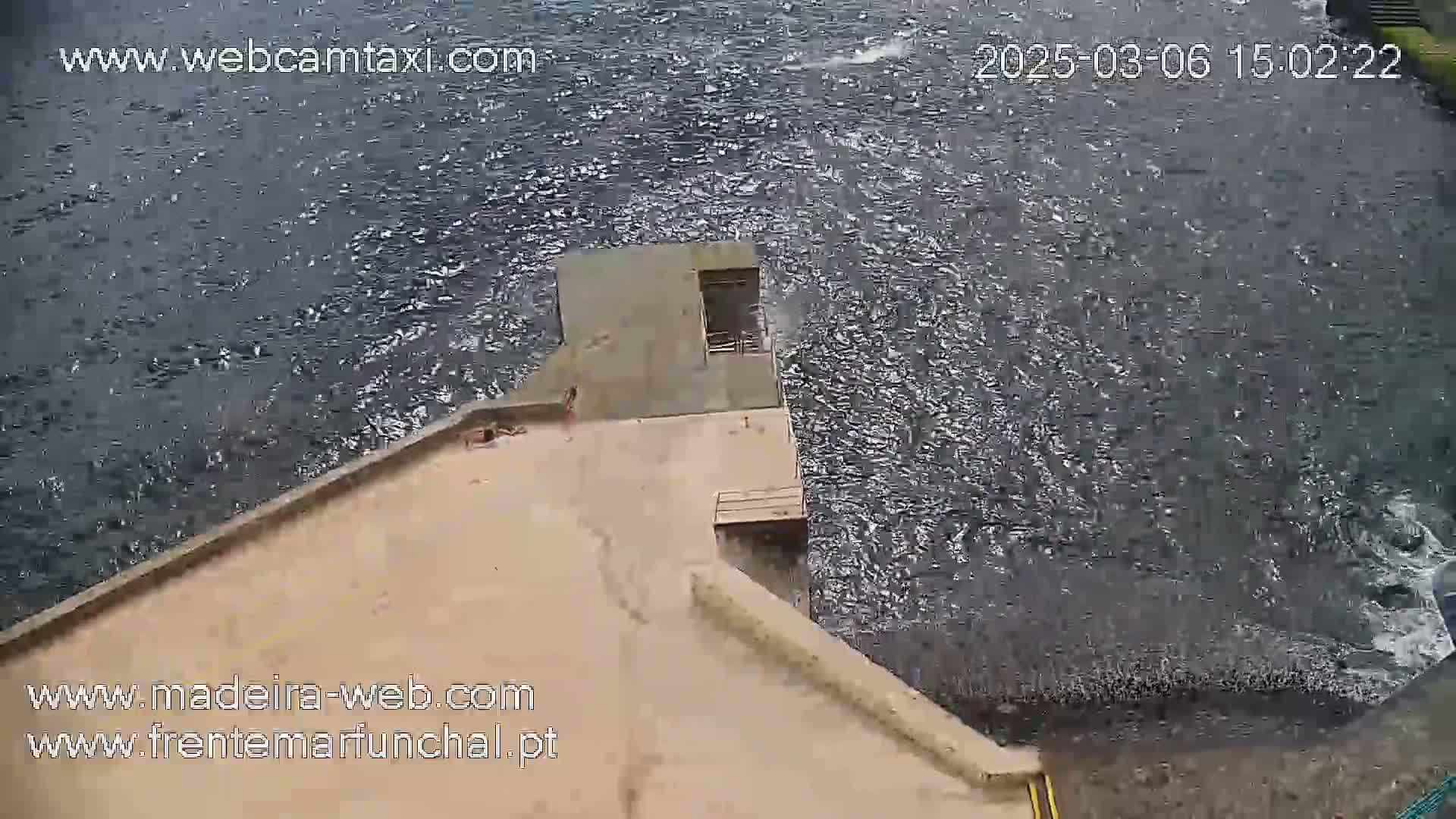 A tan concrete structure extends over a dark, choppy body of water.