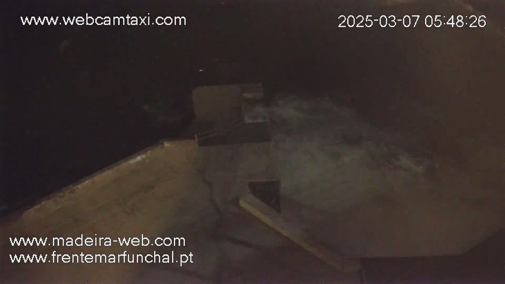 A nighttime, high-angle view shows a dark, concrete structure with water splashing against it.