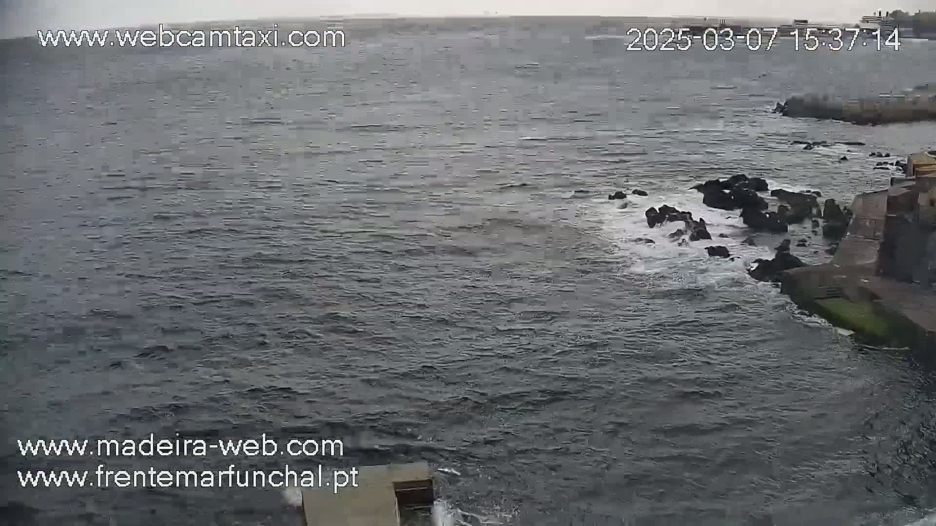 A dark, choppy ocean meets a rocky shore under an overcast sky.