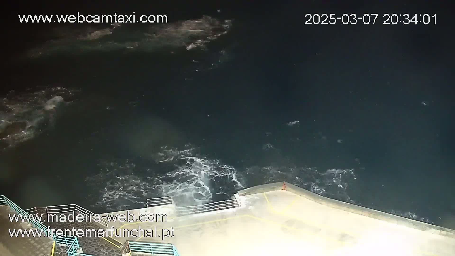 A nighttime view shows dark water with whitecaps lapping against a low concrete wall.