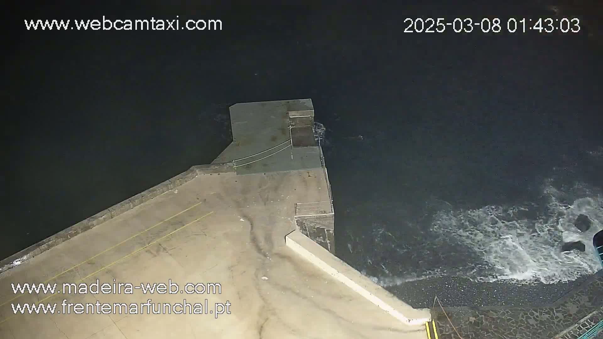 An overhead nighttime view shows a concrete structure extending into dark, wave-swept water.