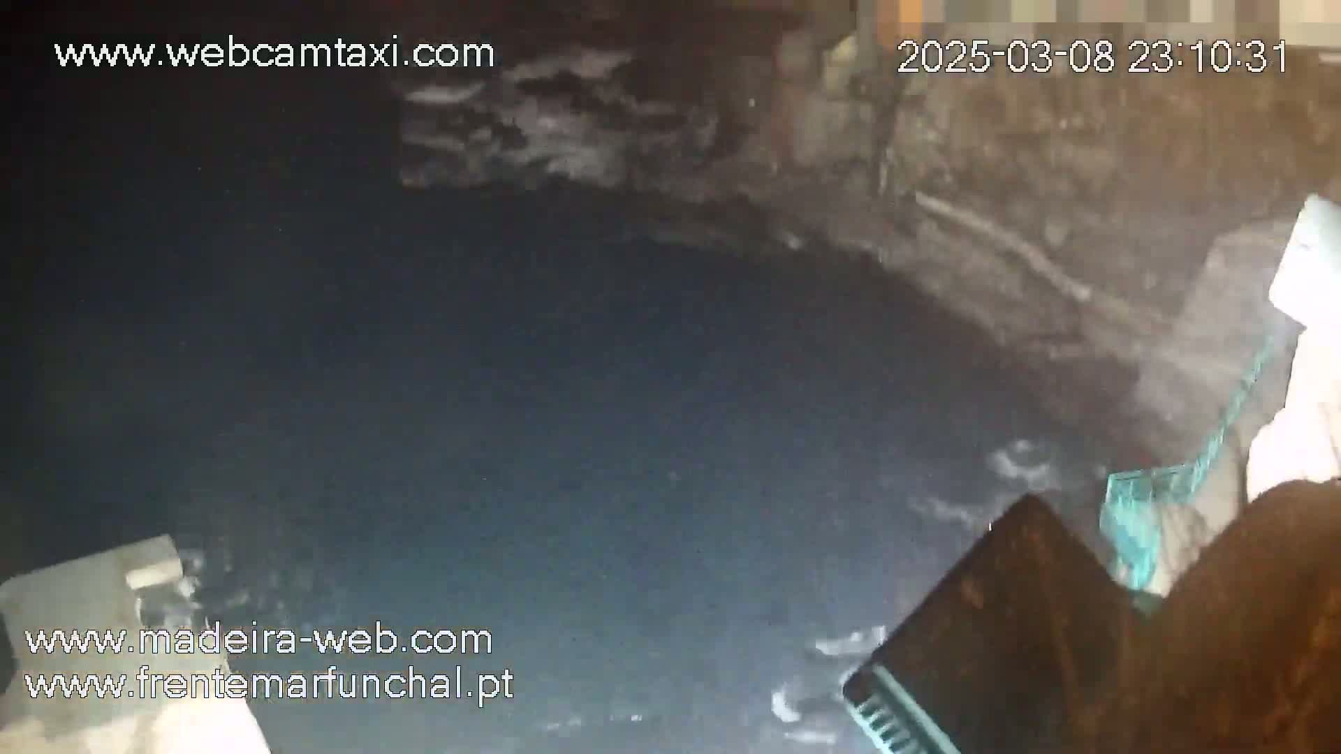 A nighttime, low-angle view shows dark water with some white foam near a dark stone structure.