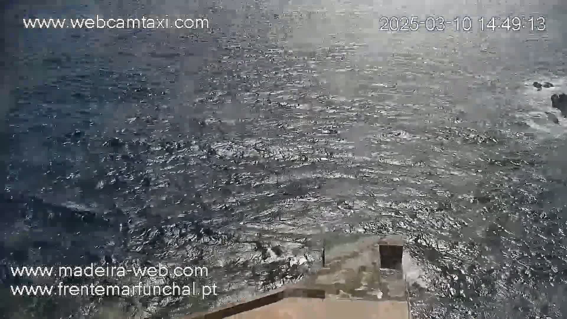A high-angle view shows dark, choppy ocean water lapping against a low stone structure.