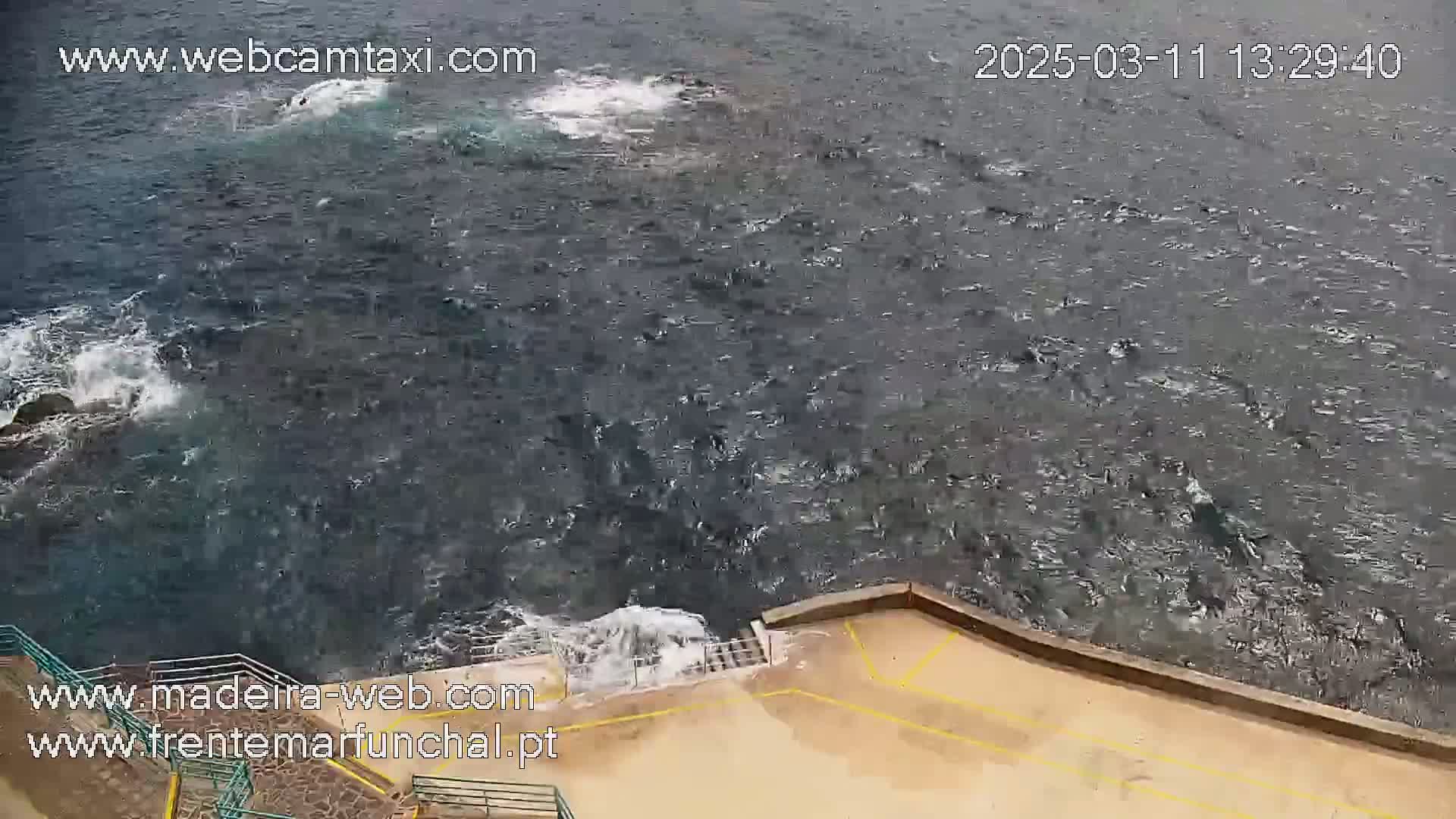 A high-angle view shows choppy dark-blue water crashing against a low stone wall.