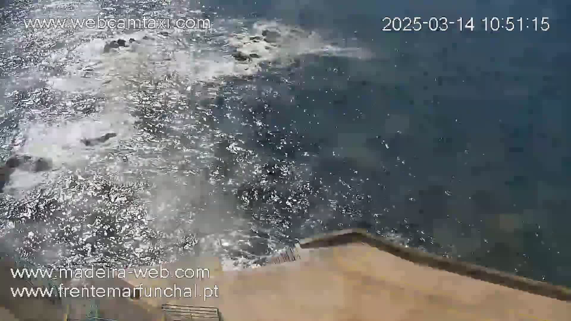 A high-angle view shows dark-blue water with whitecaps splashing against a tan surface.