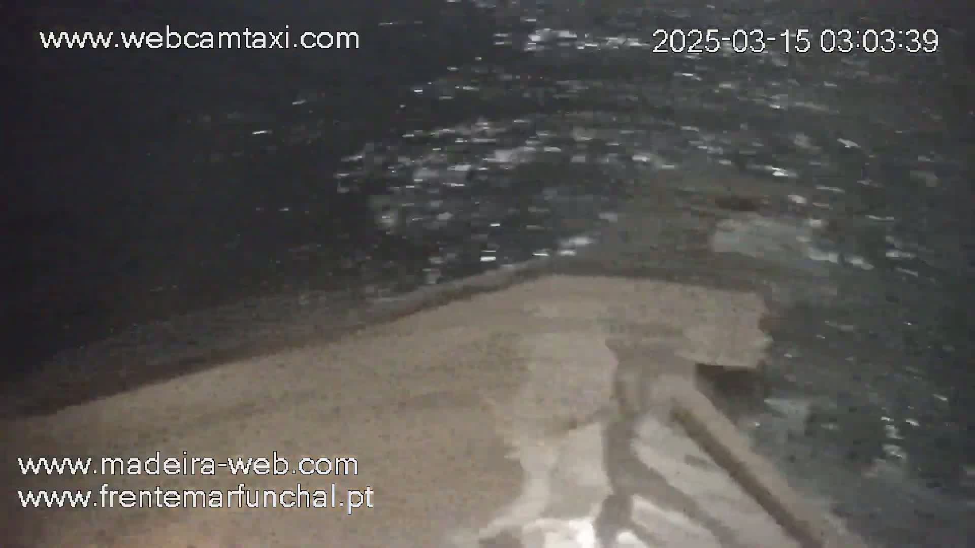 A nighttime, low-light view of dark, choppy water lapping against a sandy shore.