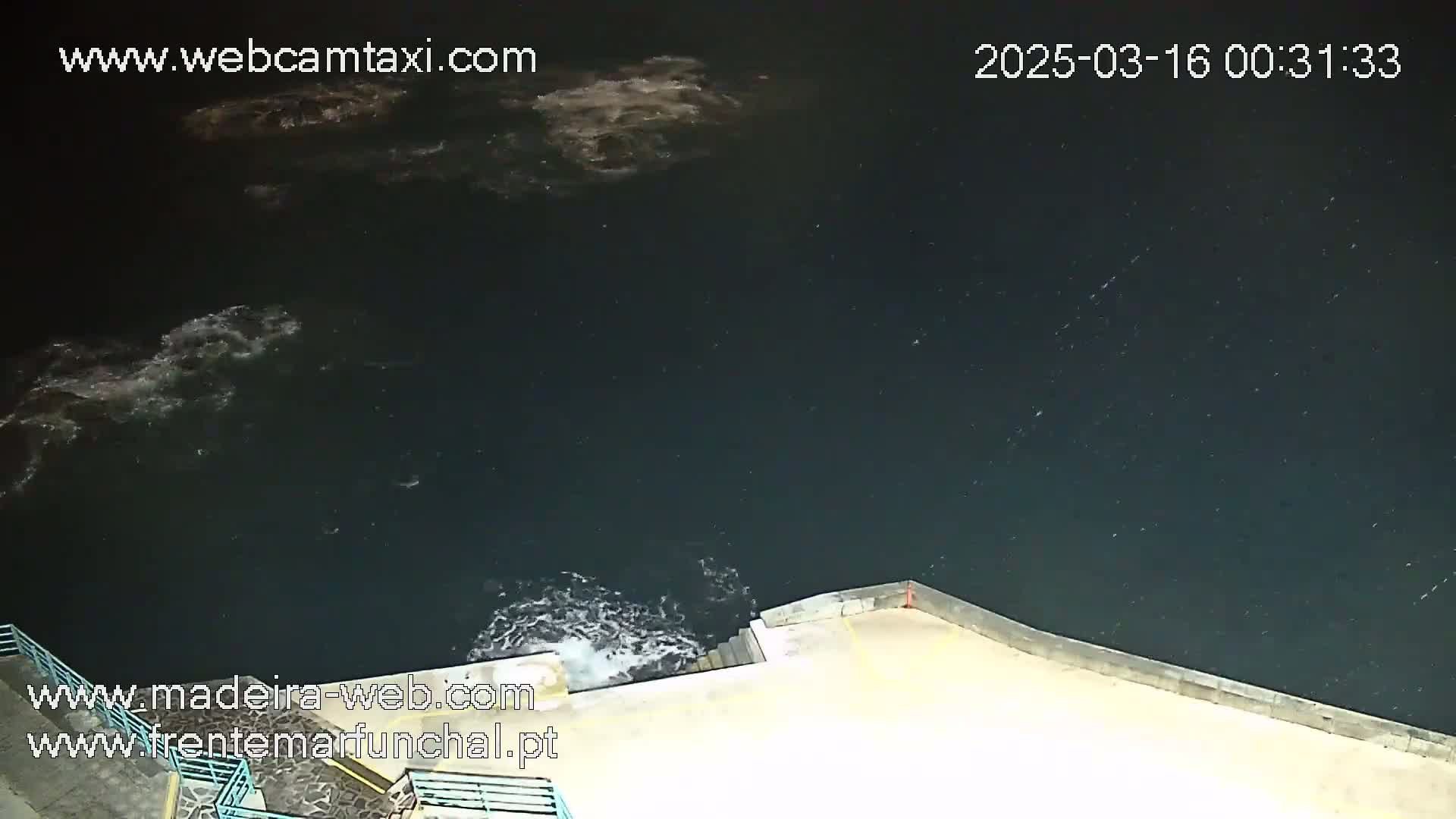 A nighttime view of dark water with some small waves lapping against a concrete wall or seawall.