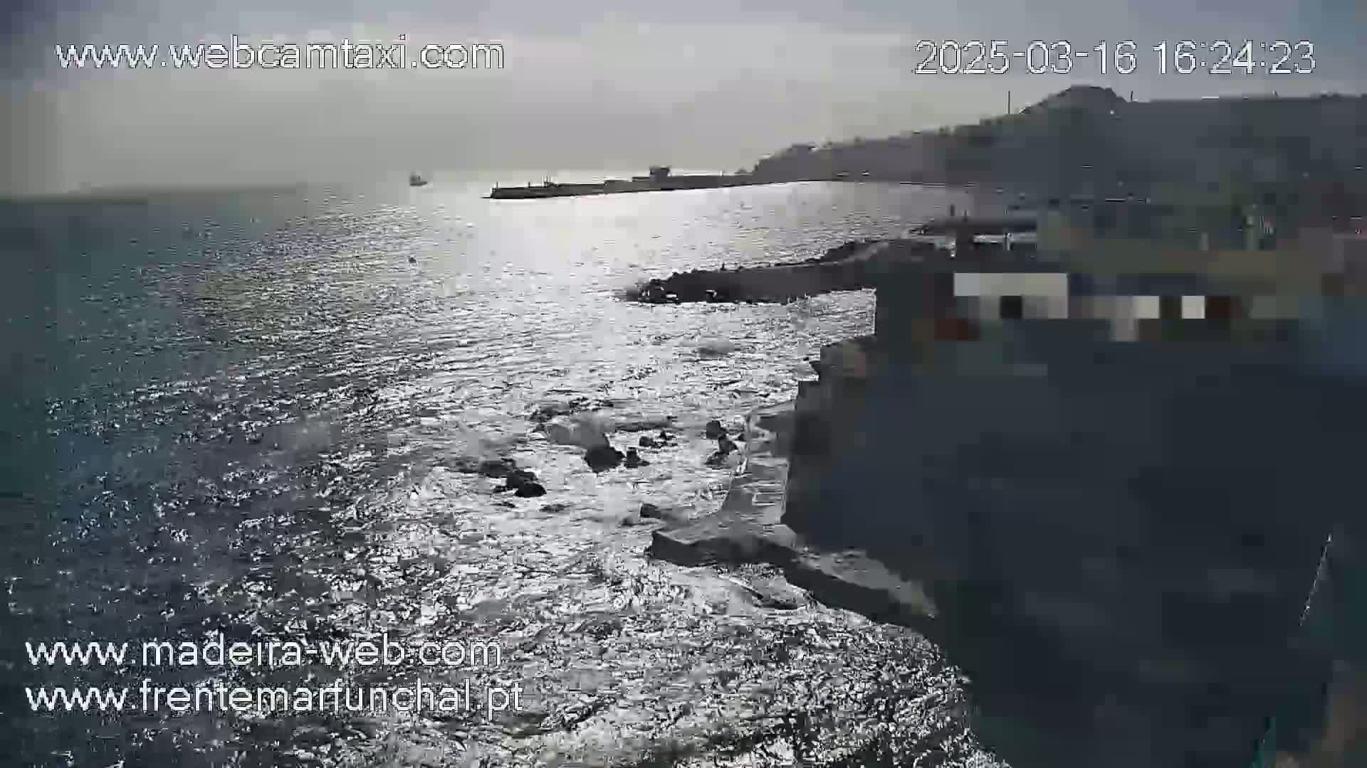 A slightly overcast day shows a rocky coastline with choppy water and a distant shoreline.