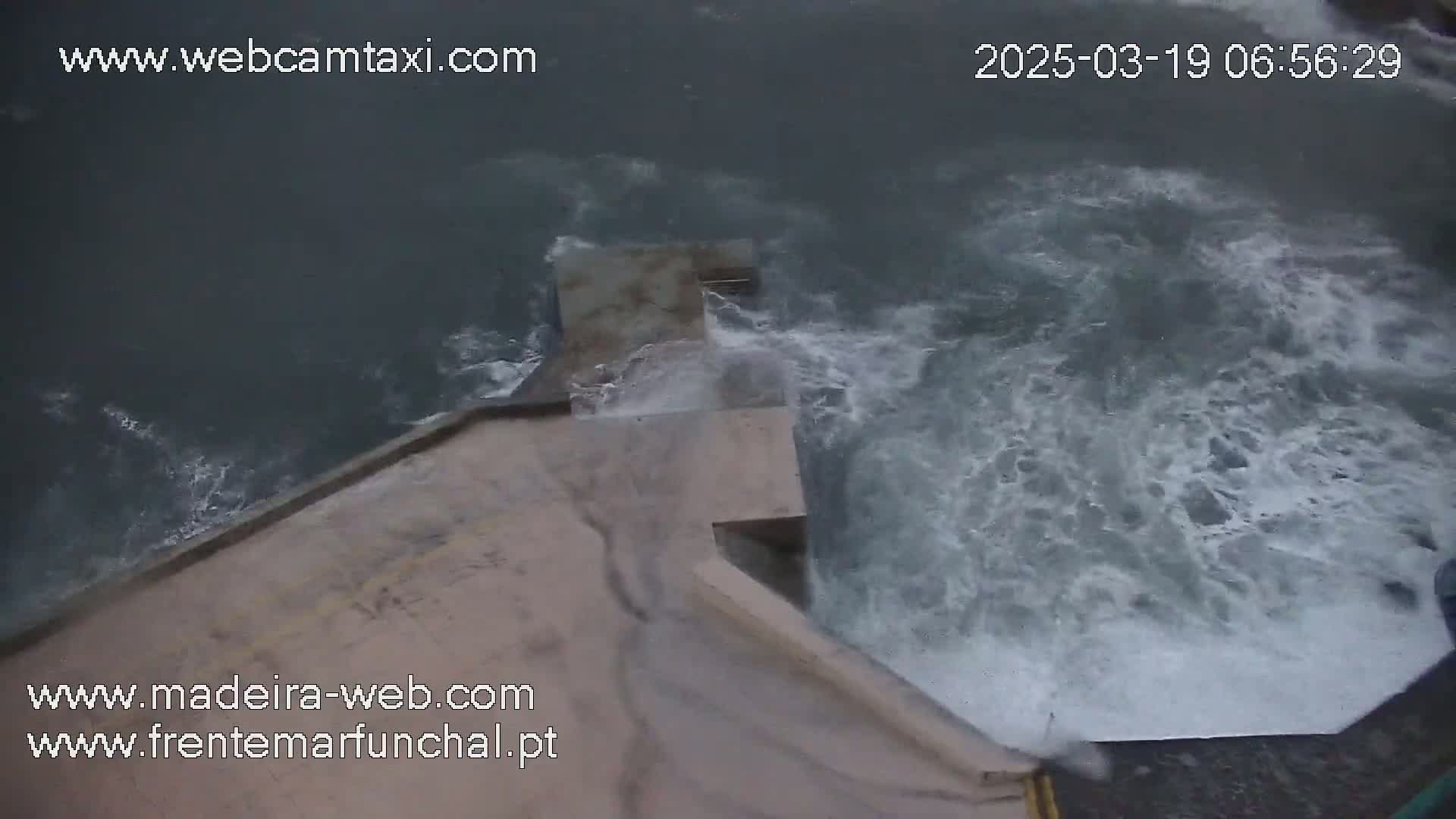 Turbulent water crashes against a concrete structure, likely a seawall or dam.