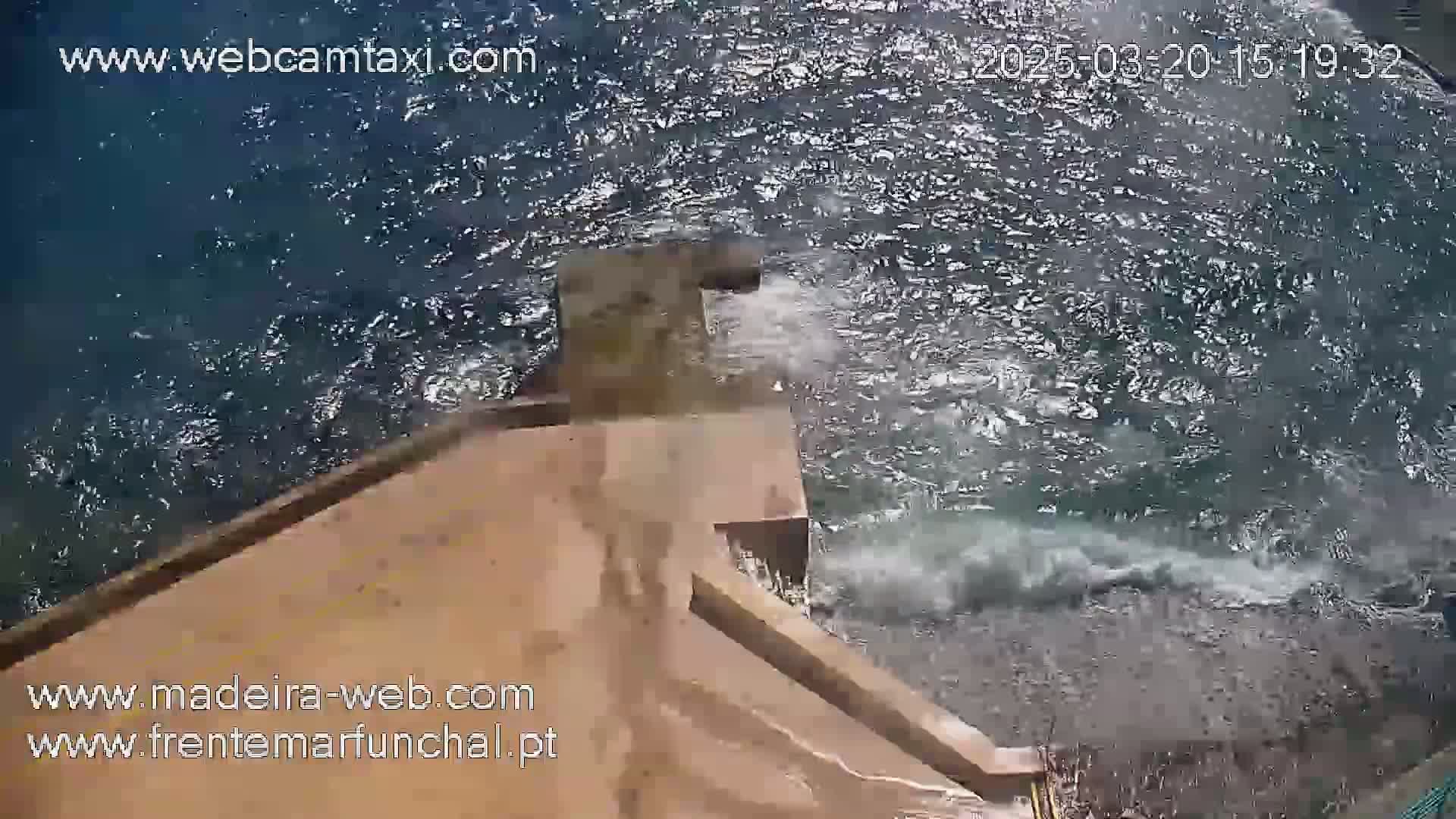 Water splashes against a tan concrete structure extending into a choppy sea.