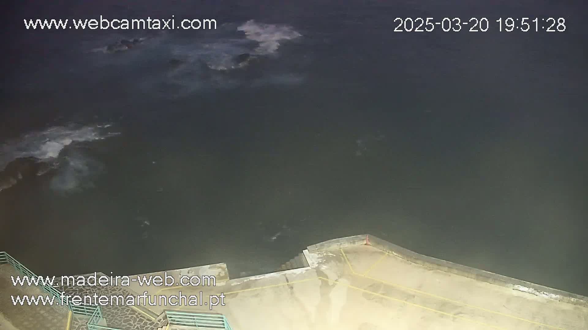A nighttime view of dark ocean water with small waves lapping against a concrete seawall.