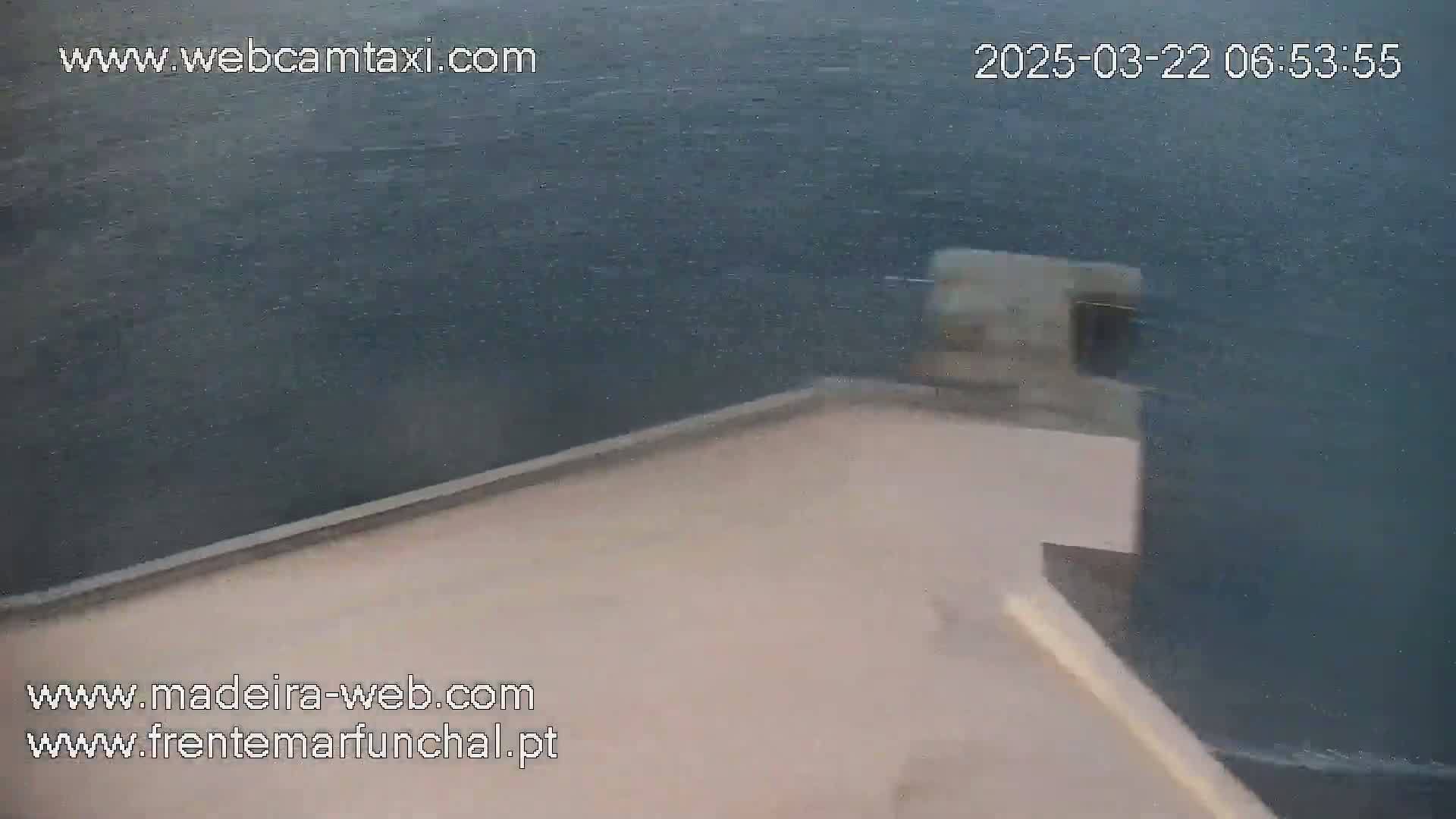 A high-angle view shows a light beige surface next to a dark body of water on a windy day.