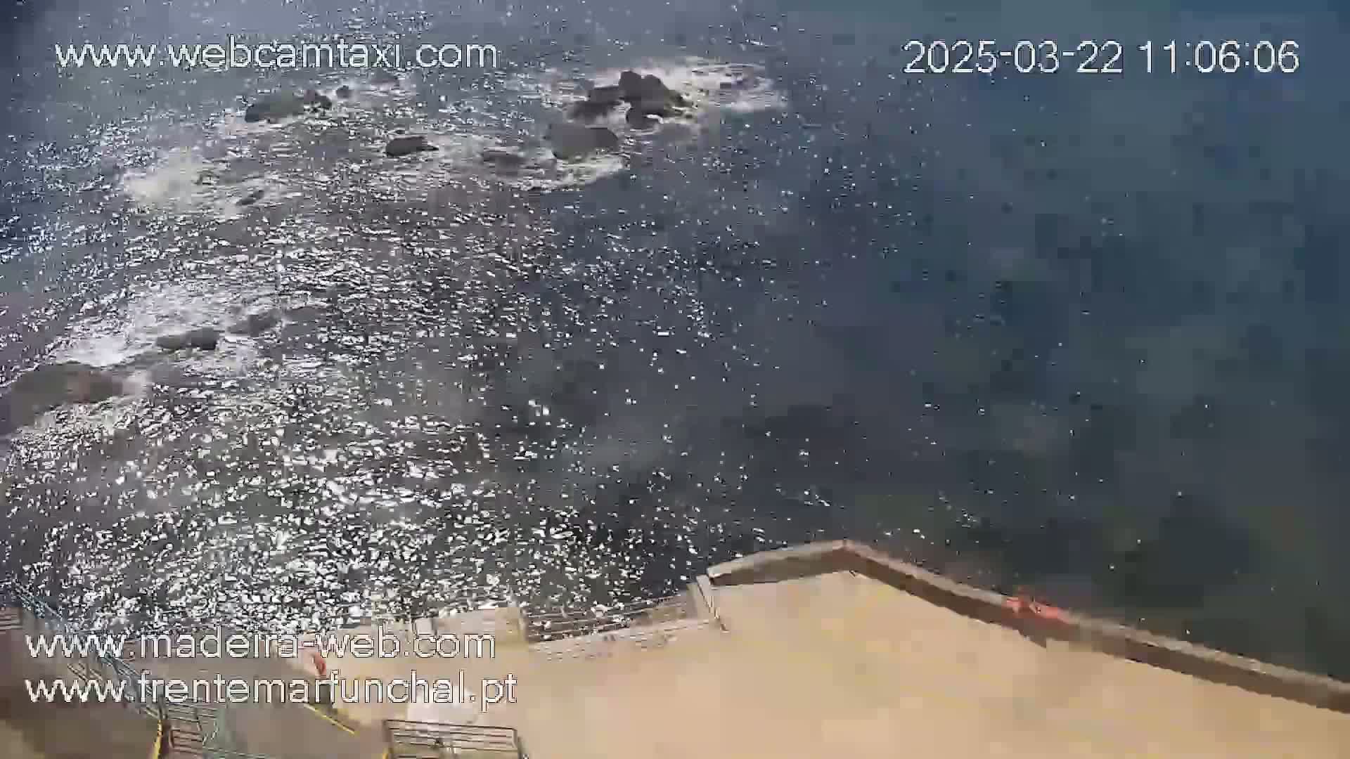 A high-angle view shows choppy water near a stone wall on a sunny day.