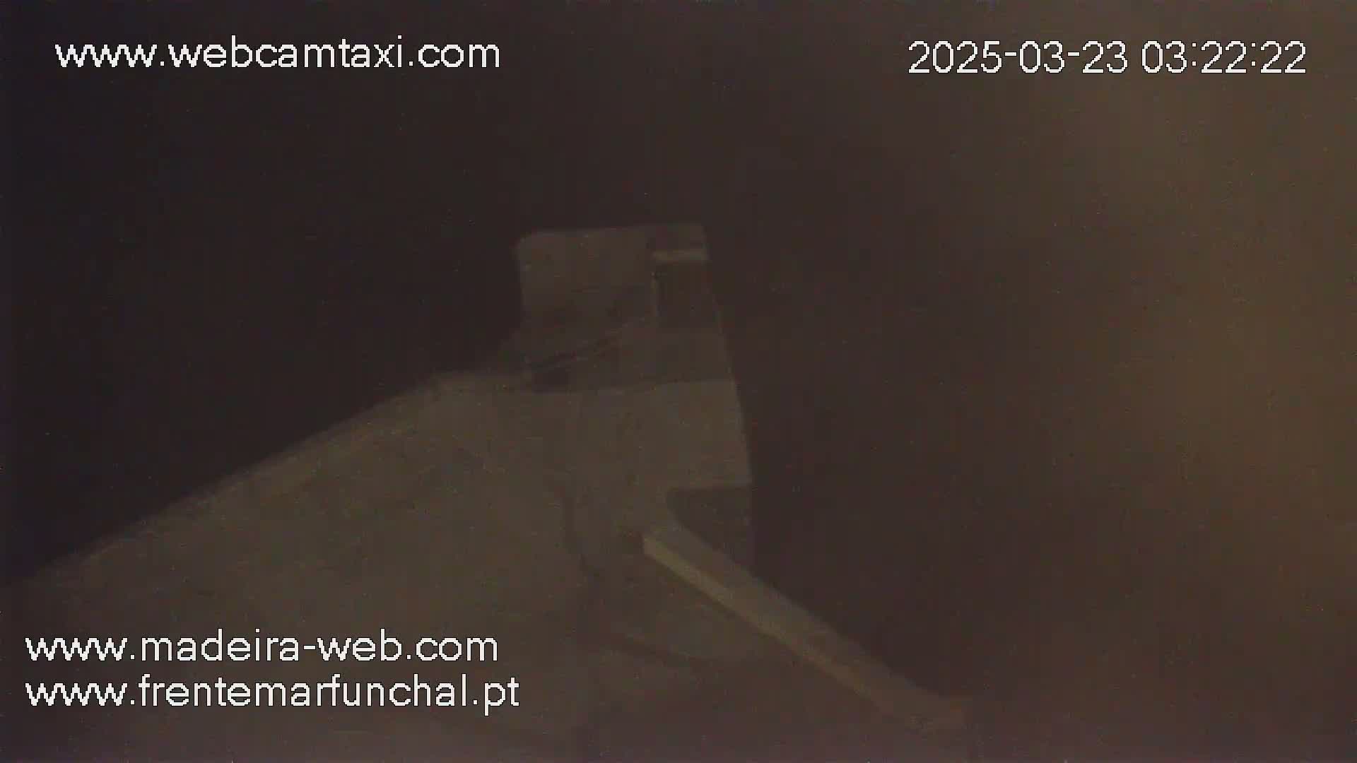 A dark, nighttime image shows a portion of a structure, possibly a building or wall, illuminated faintly.