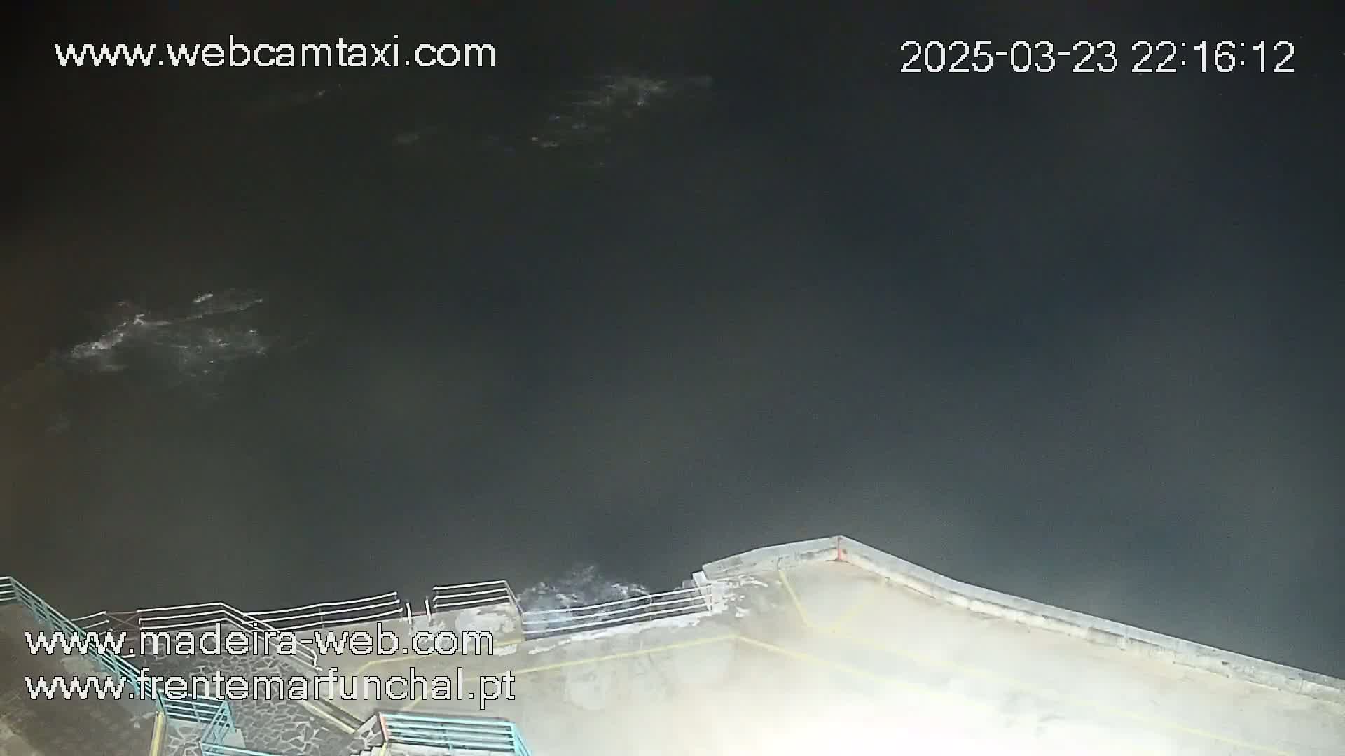 A nighttime, high-angle view shows dark water with some whitecaps near a cement waterfront with railings.
