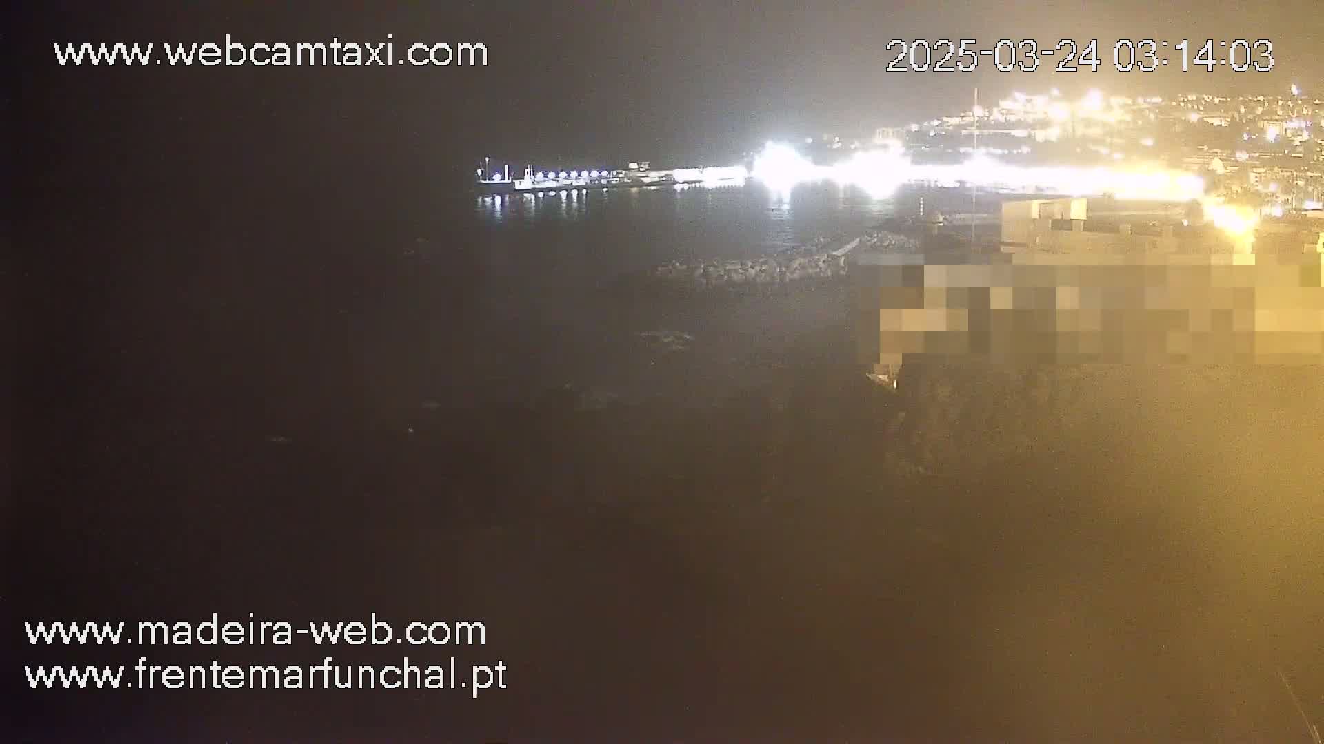 A nighttime view of a harbor with city lights across the water, under hazy or foggy conditions.