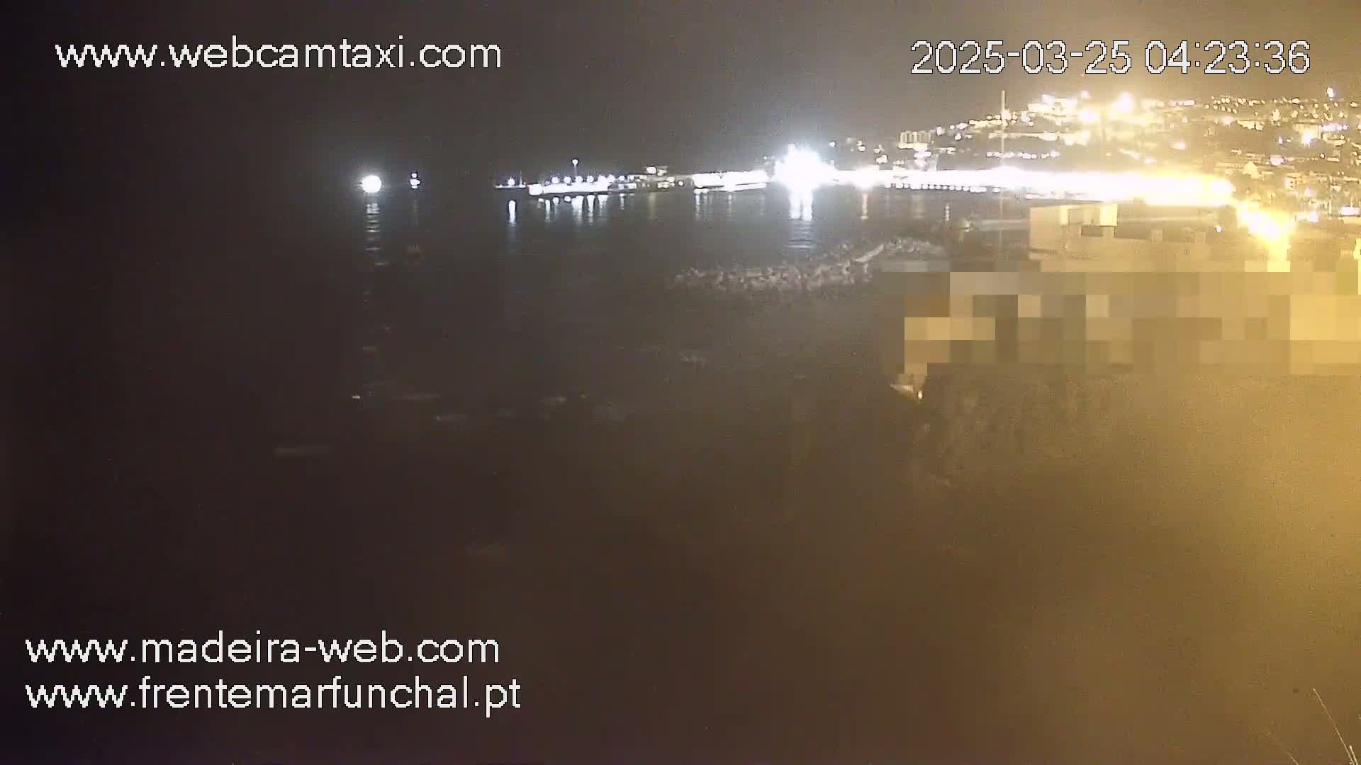 A nighttime, low-light view of a dark body of water with a brightly lit city in the background.