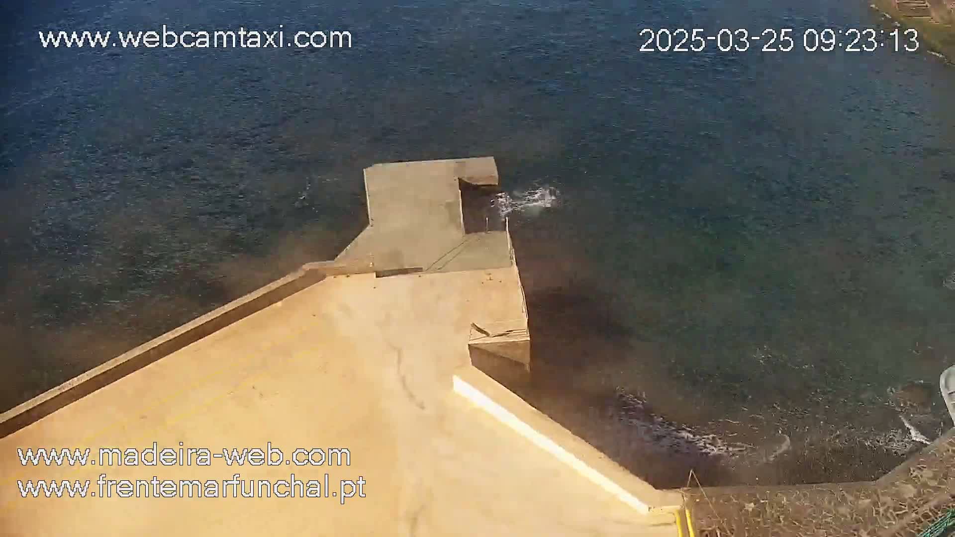 A tan concrete platform extends over dark-blue water, where small waves lap against its edge.