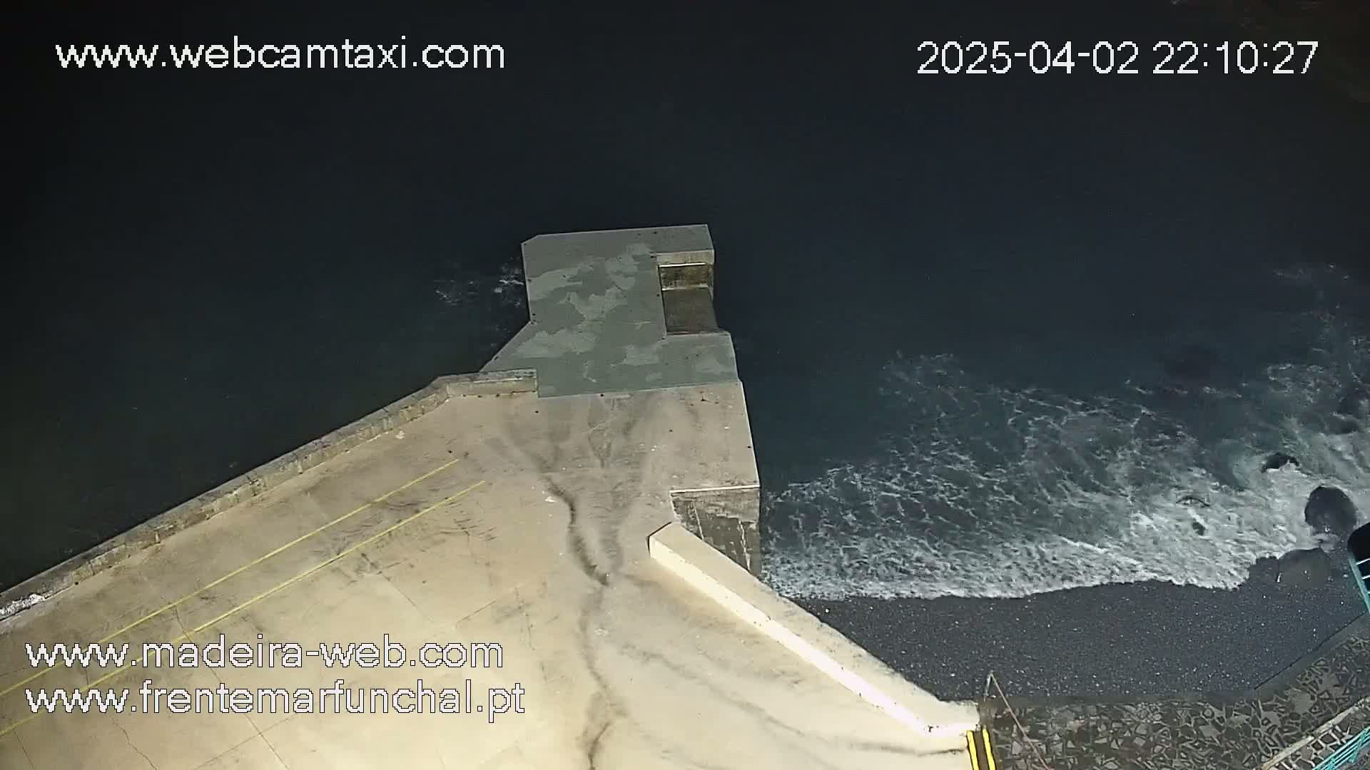 An overhead nighttime view shows dark water lapping against a concrete structure on a shoreline.
