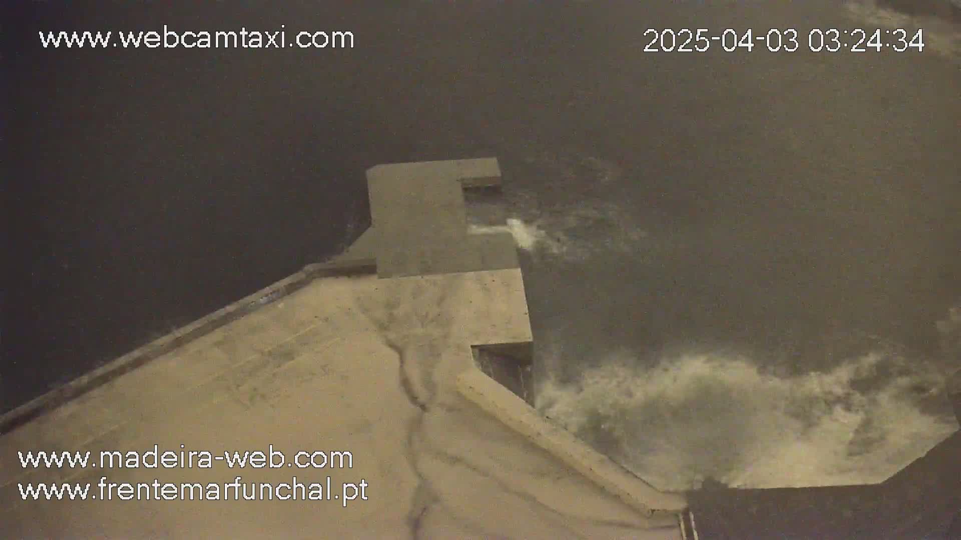 A high-angle nighttime view shows water flowing over a concrete structure into dark water.