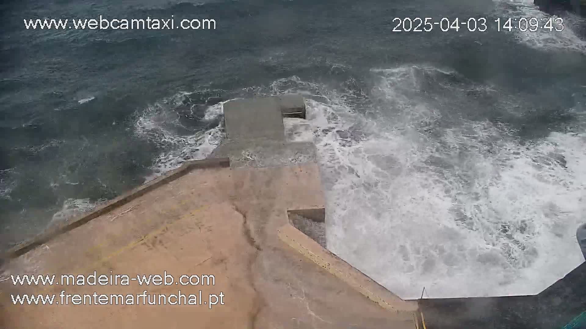 A concrete structure on a coastline is being battered by large, powerful waves in stormy weather.