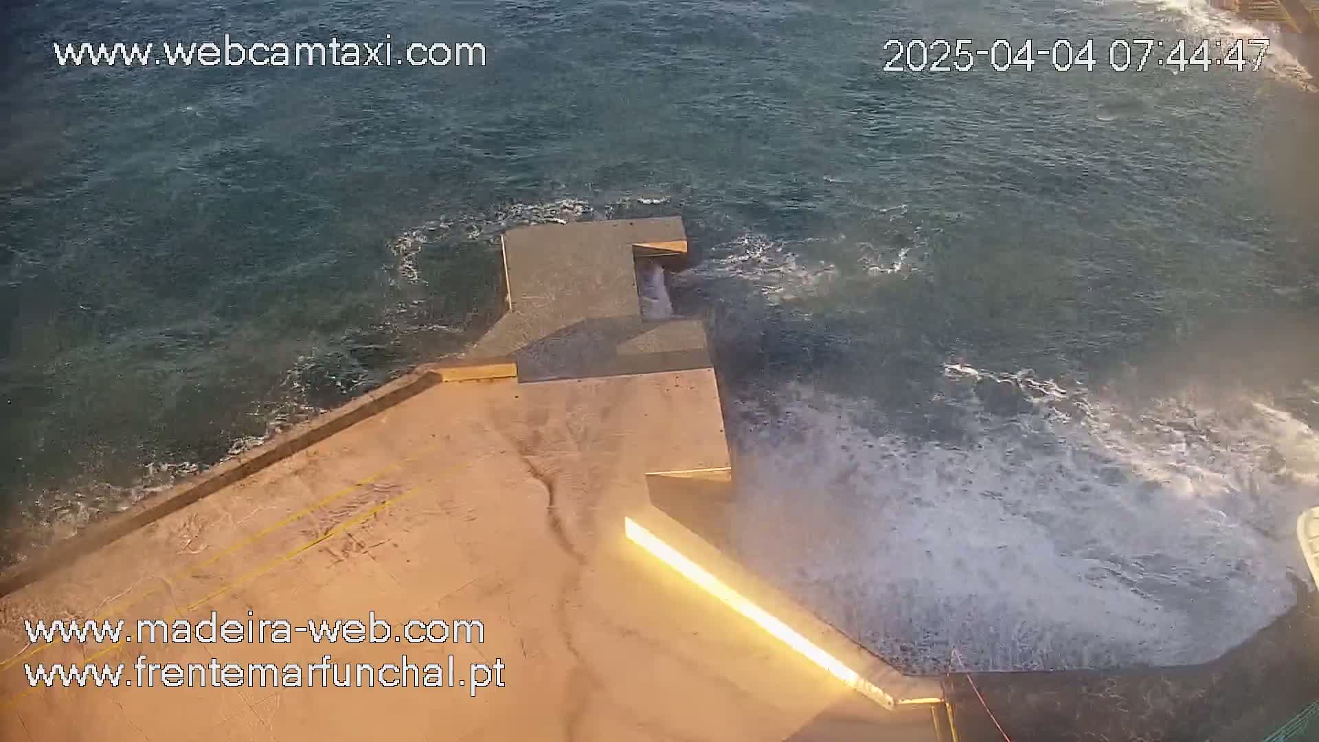Waves crash against a concrete structure extending into a dark-colored sea.