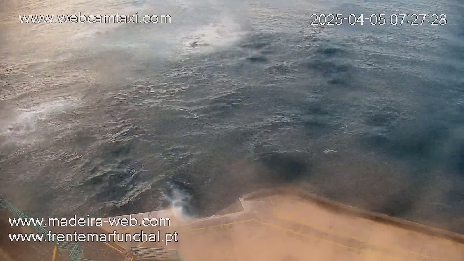 A high-angle view shows a choppy, dark-grey sea with some mist or spray, partially obscuring a tan-colored structure at the bottom of the frame.