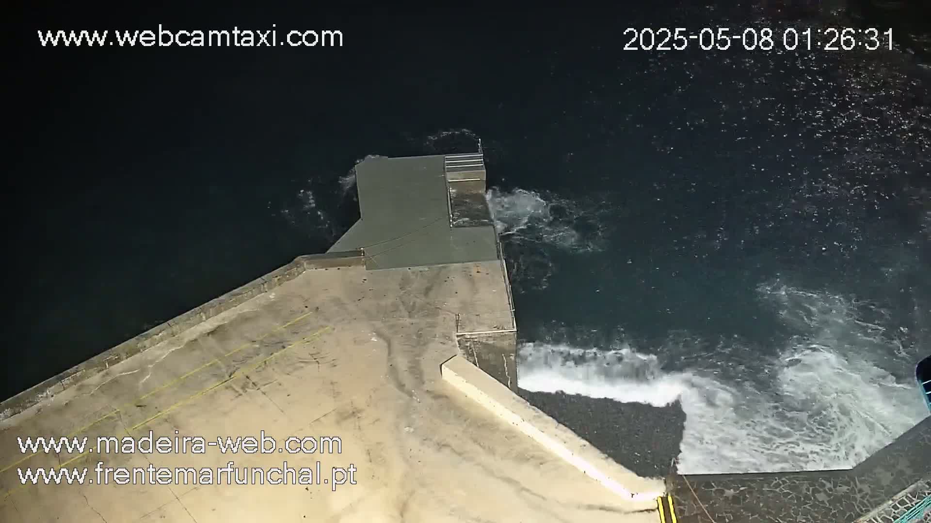 A nighttime overhead view shows a concrete structure extending into dark, wavy water.