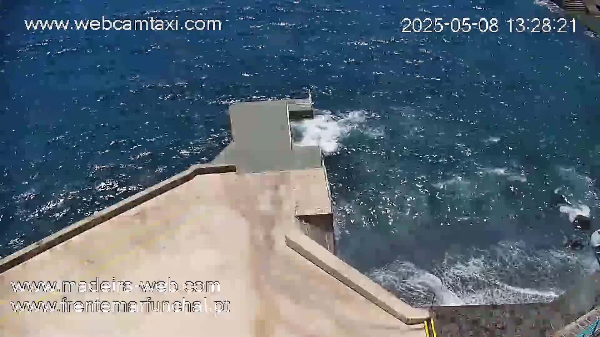 A tan concrete structure extends over a dark blue ocean with small waves crashing against it.