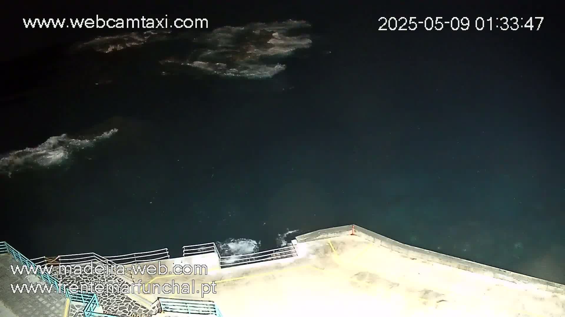 A dark, nighttime view of a body of water with small waves lapping against a concrete wall.