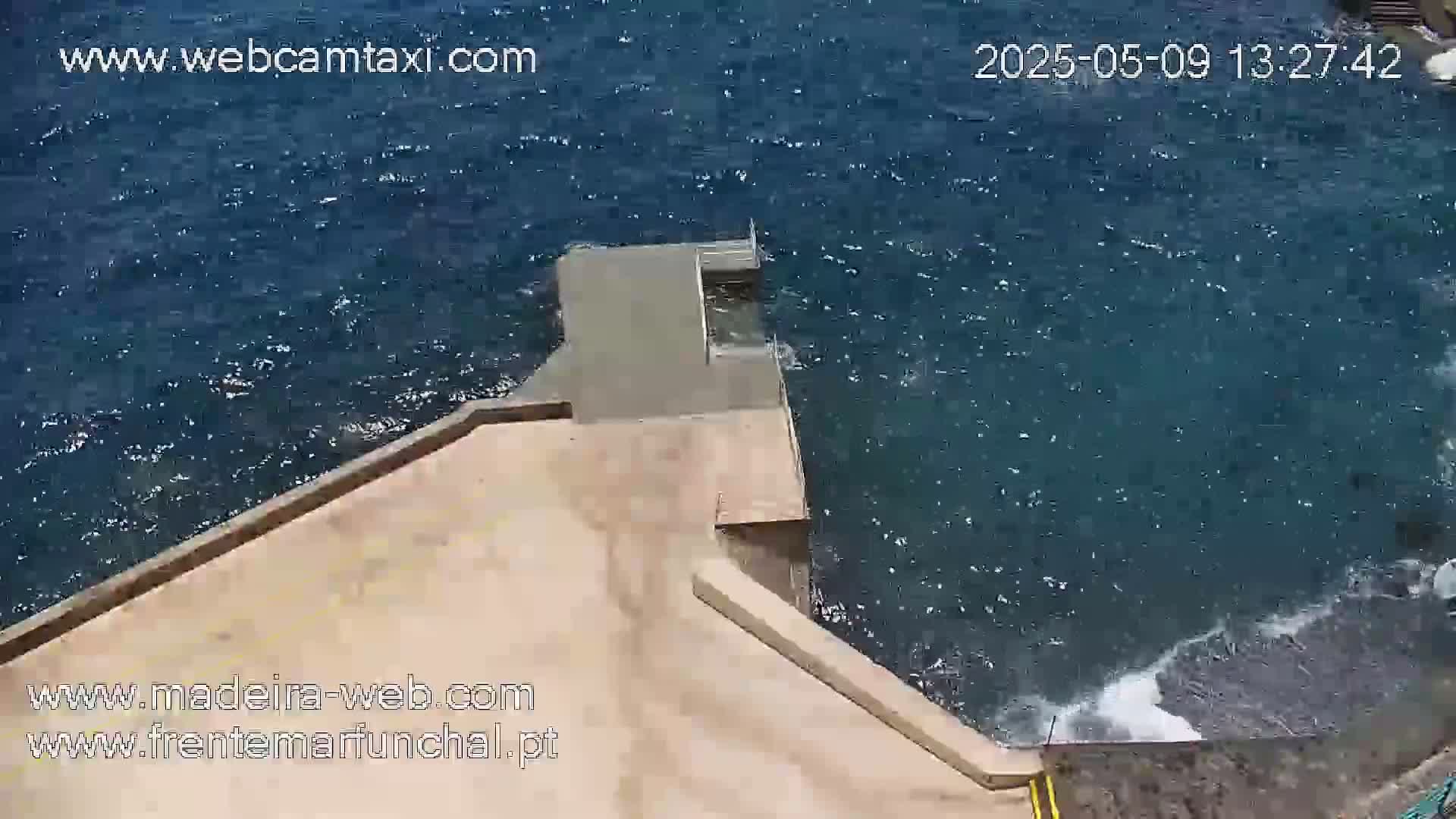 A tan concrete platform extends over dark-blue water with small waves.