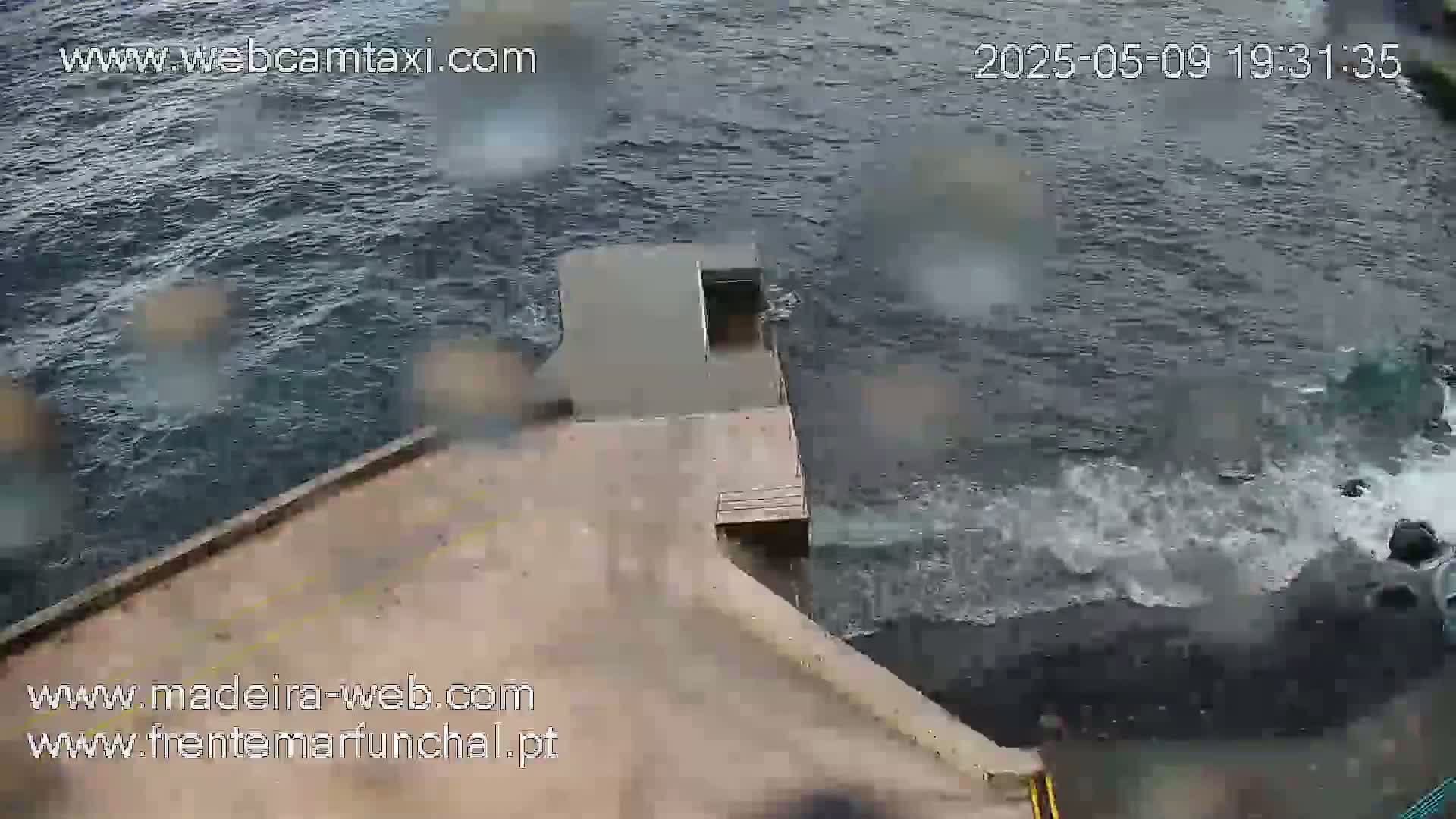A concrete dock extends over dark, choppy water during a rainy day.