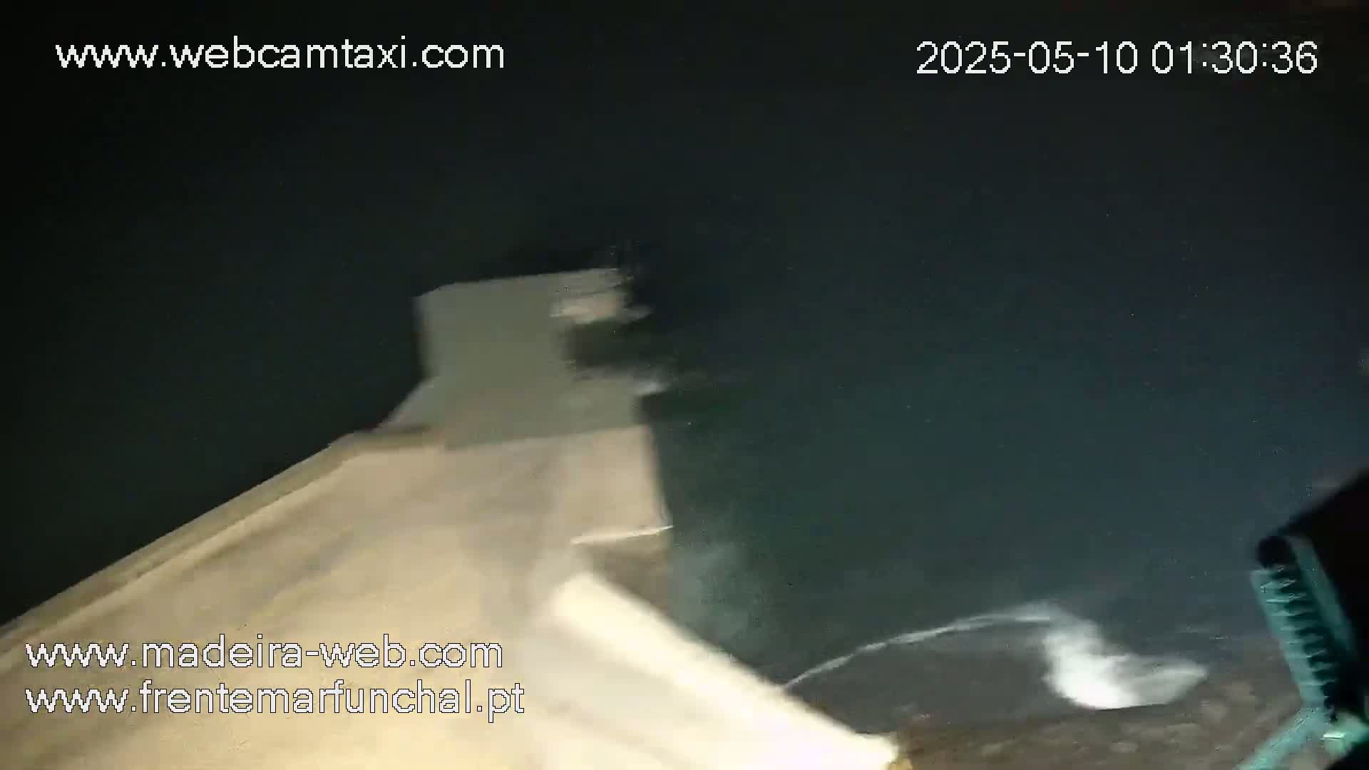 A nighttime, dark-colored body of water is seen from a high vantage point, with a light-colored structure partially visible in the foreground.