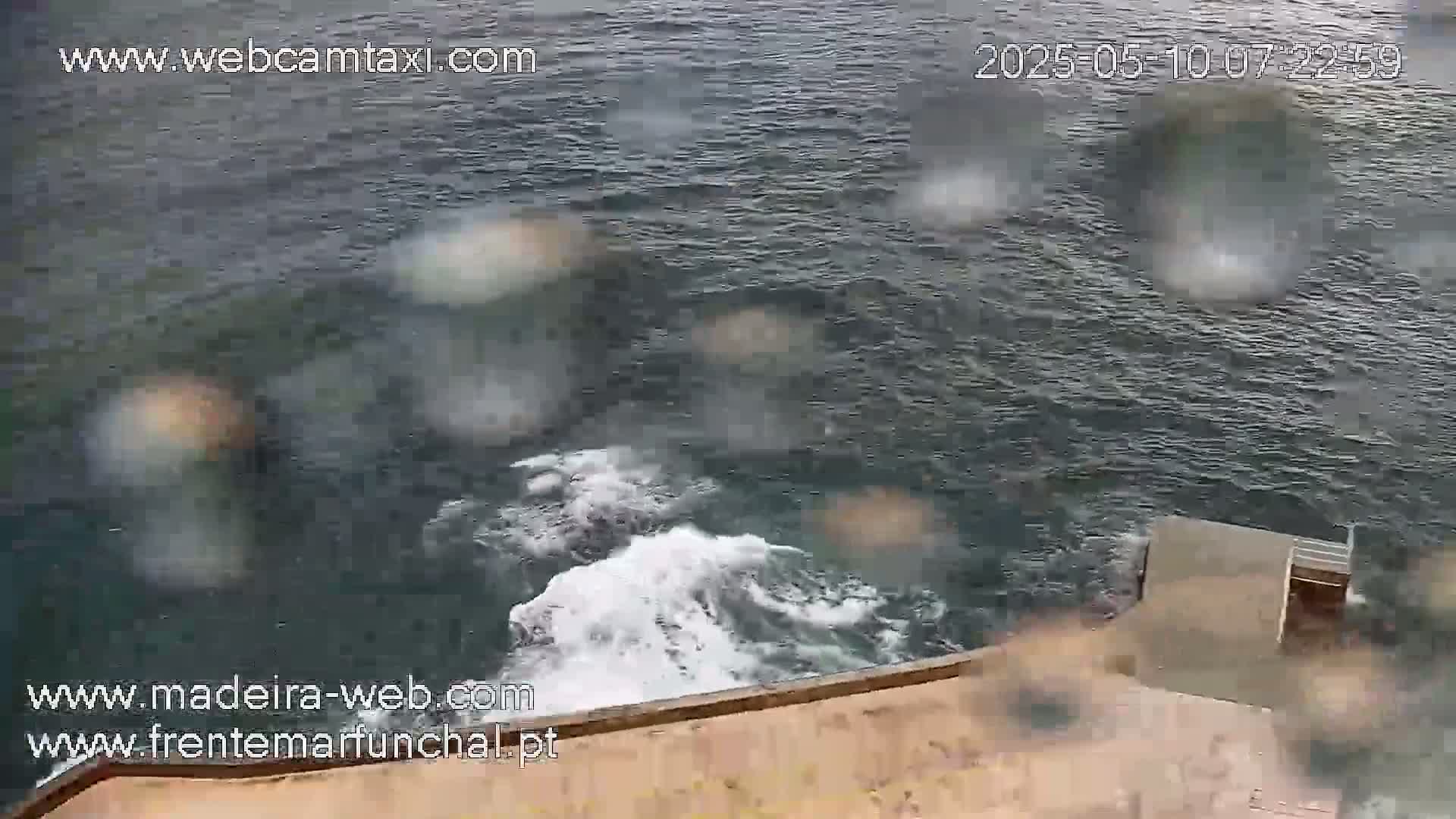 A rain-spattered view of dark, choppy water crashing against a tan concrete structure.