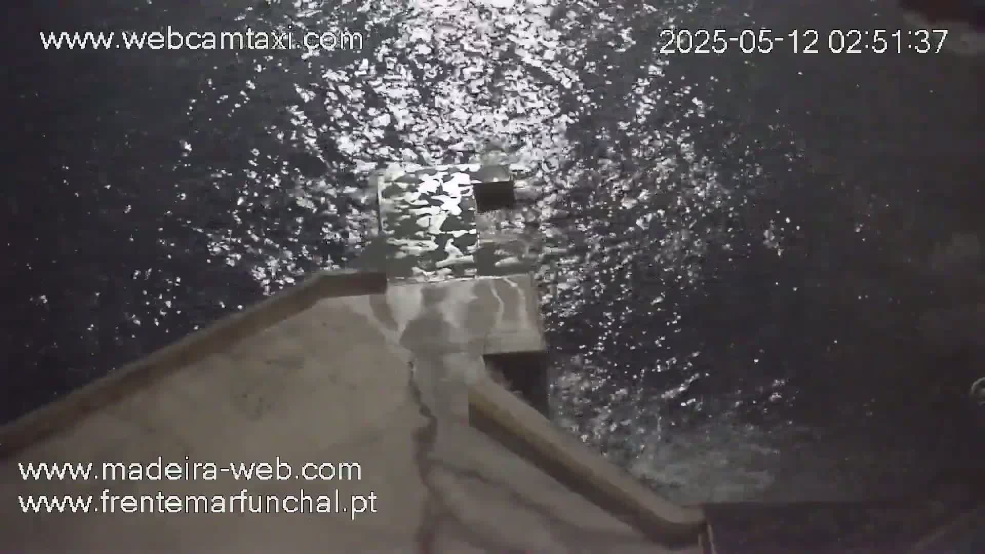 A high-angle, nighttime view shows dark, choppy water splashing against a light-colored concrete structure.
