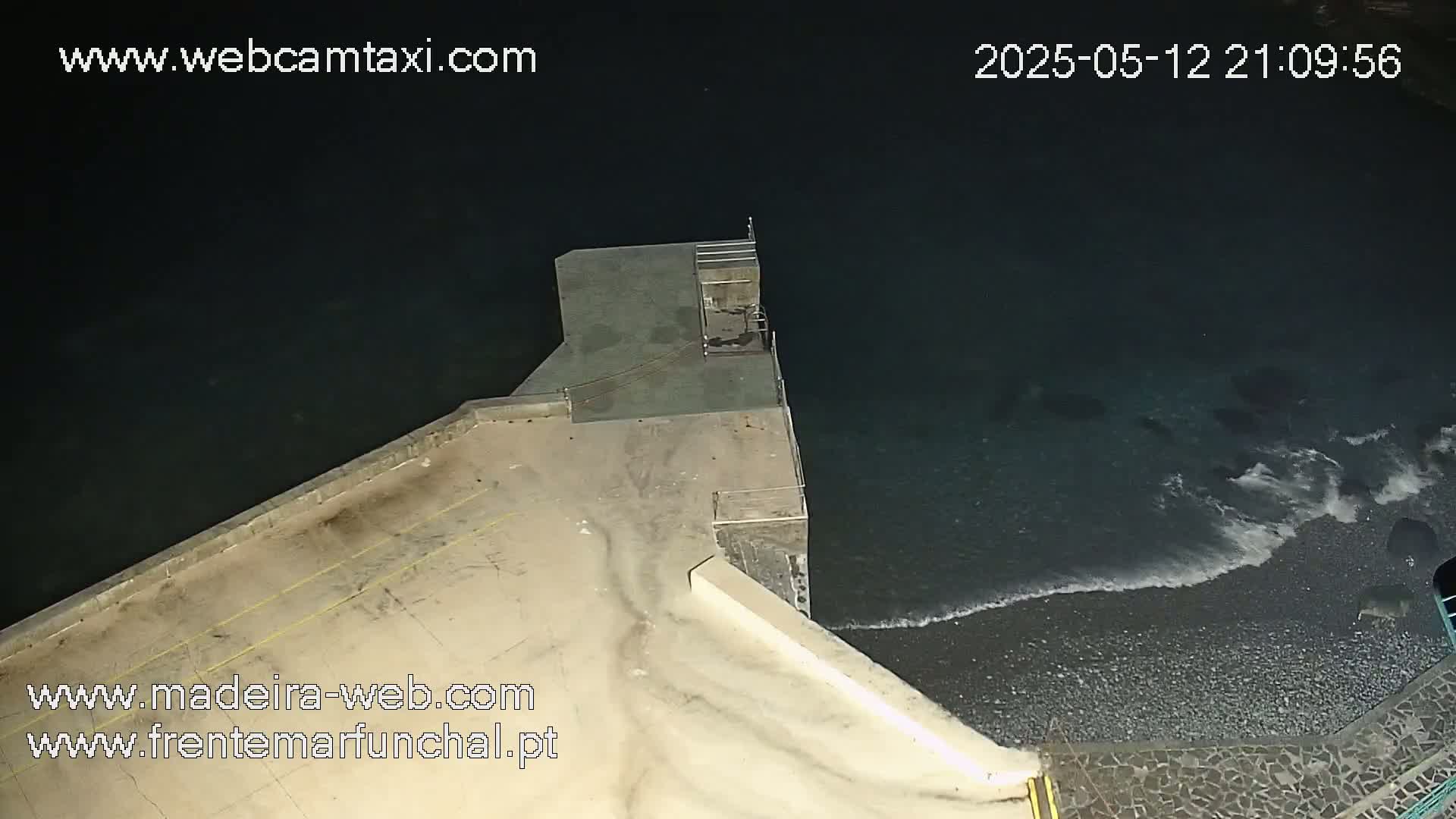 A nighttime, high-angle view shows a concrete pier extending into dark, wavy ocean water.