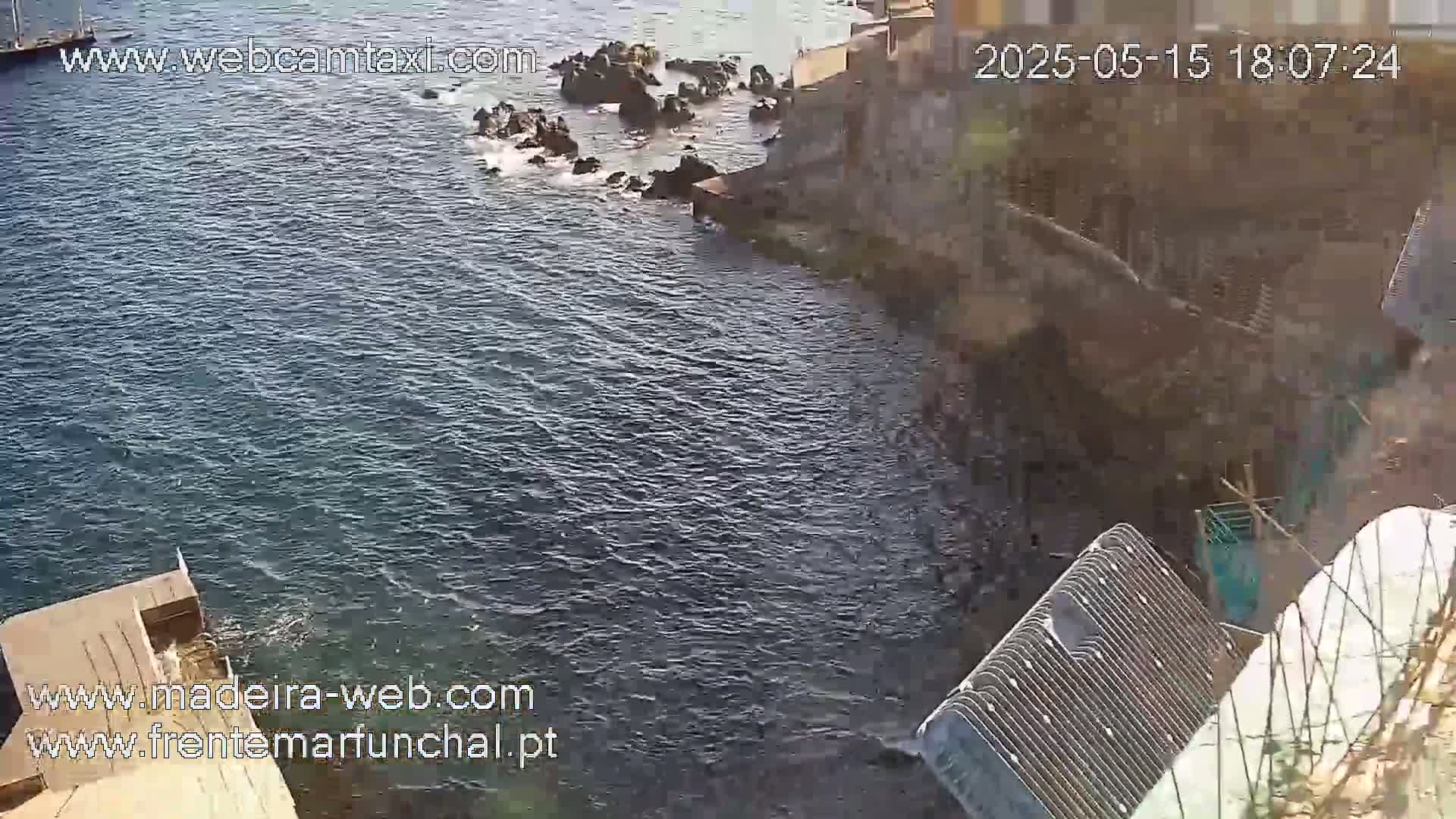 Dark blue water laps against a rocky shoreline next to a stone structure on a sunny day.