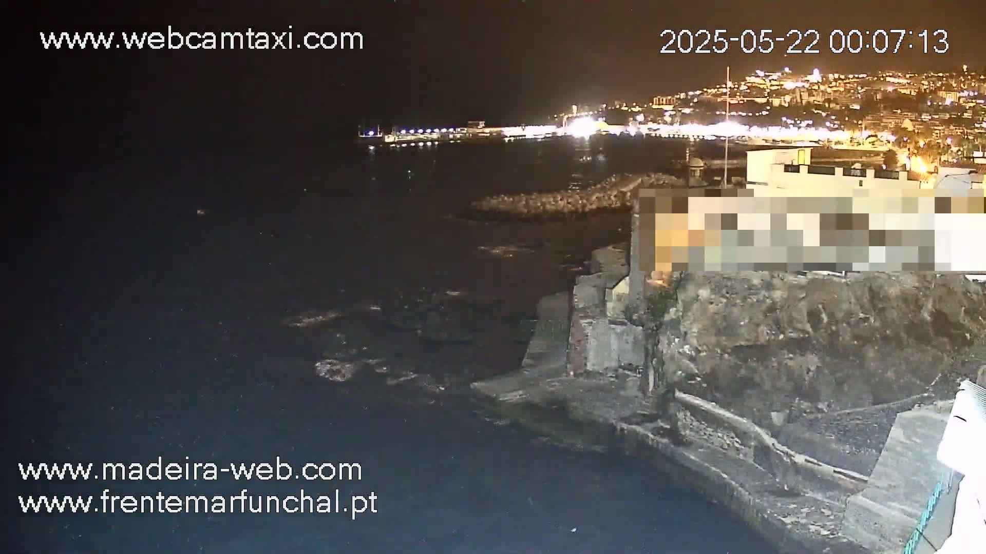 A nighttime coastal scene shows dark water lapping against a rocky shore, with a city's lights visible in the distance.