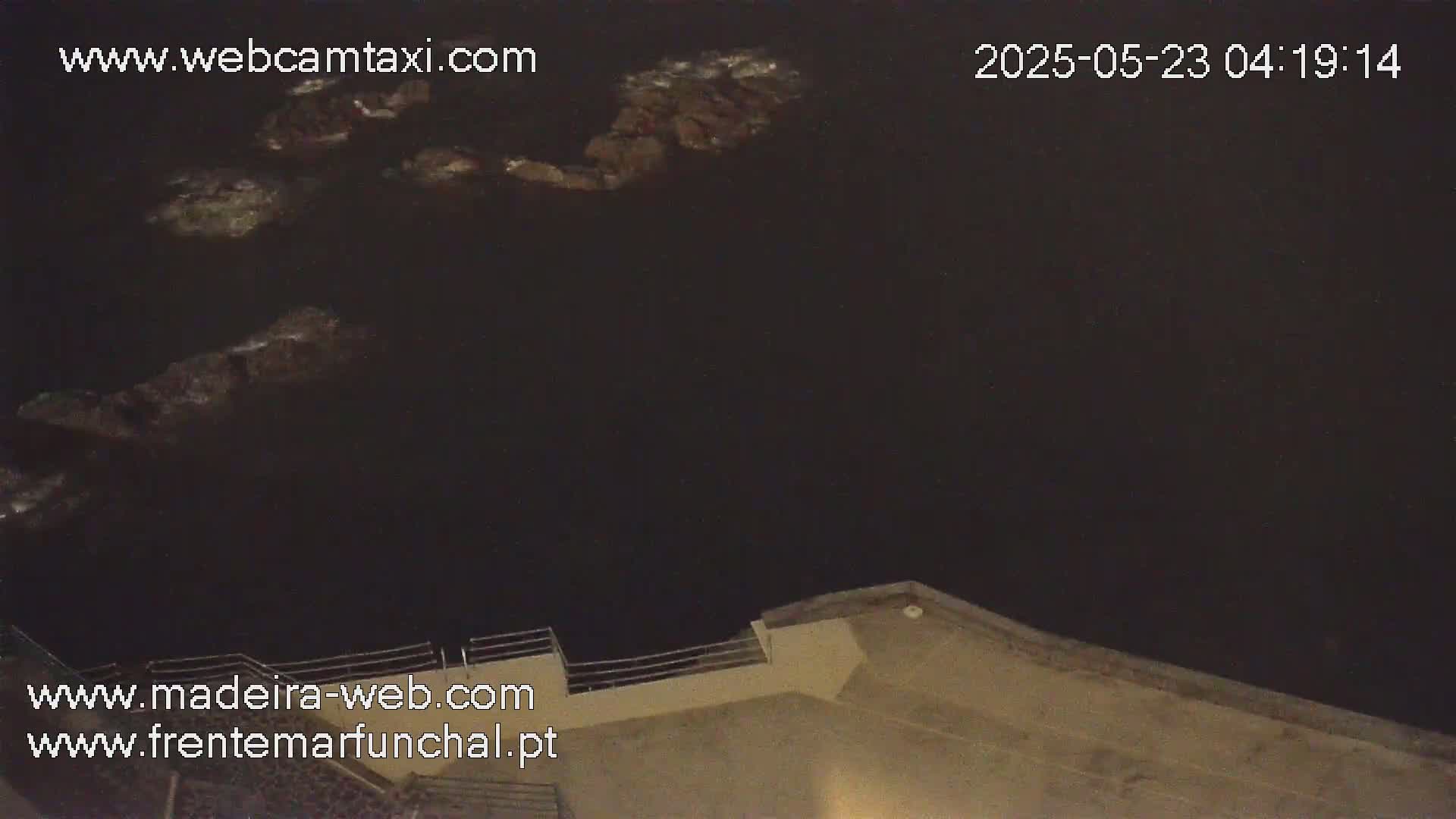 Dark, nighttime view of dark water with some rocks partially visible near a building's edge.