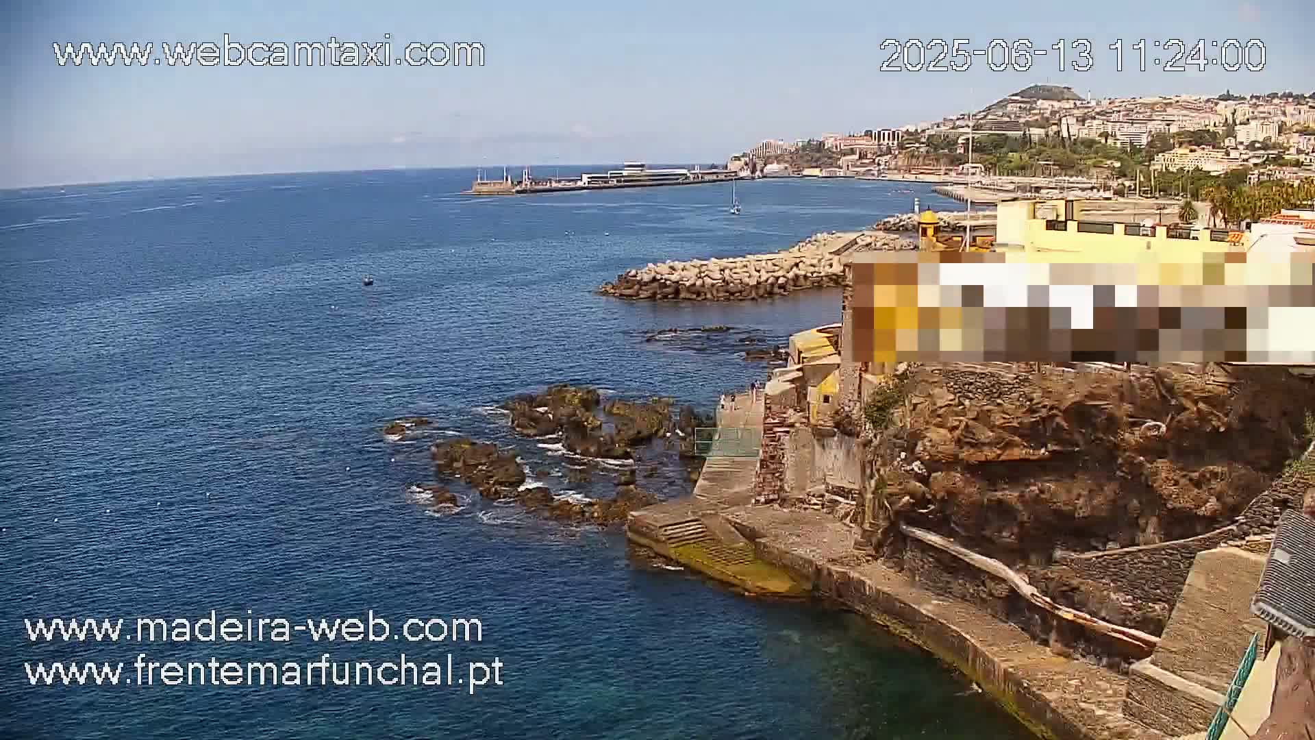 A rocky coastline with buildings and a calm, blue ocean under a clear sky.