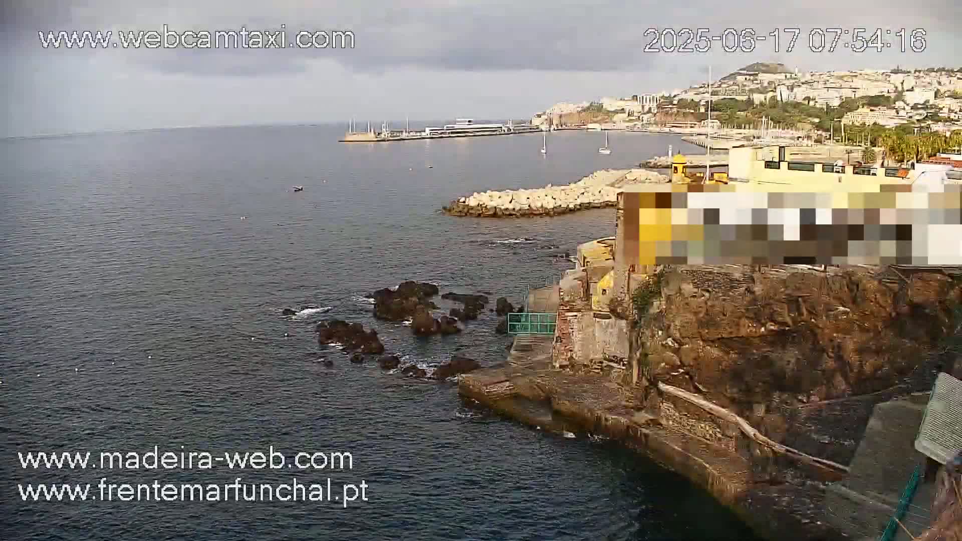A rocky coastline with a calm ocean and a town visible in the distance under overcast skies.