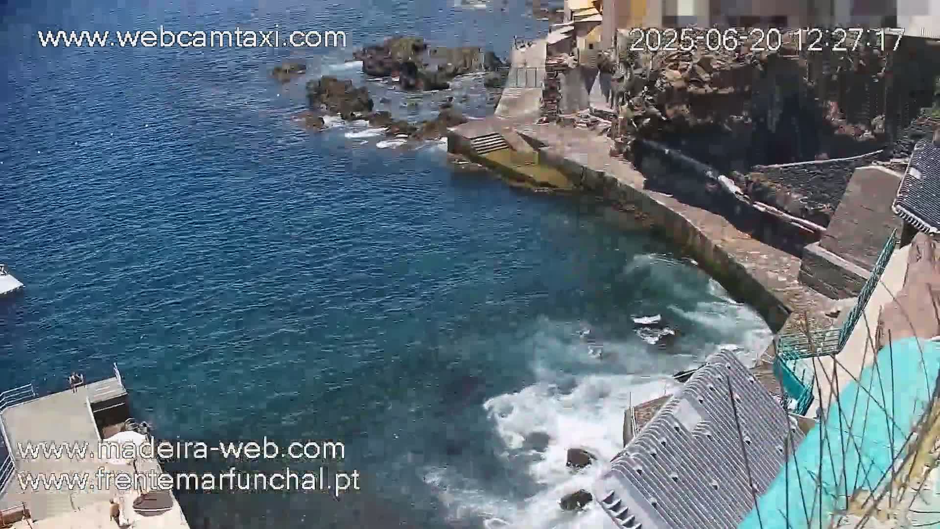 A rocky coast with a small inlet of churning blue water is seen from an elevated viewpoint on a sunny day.