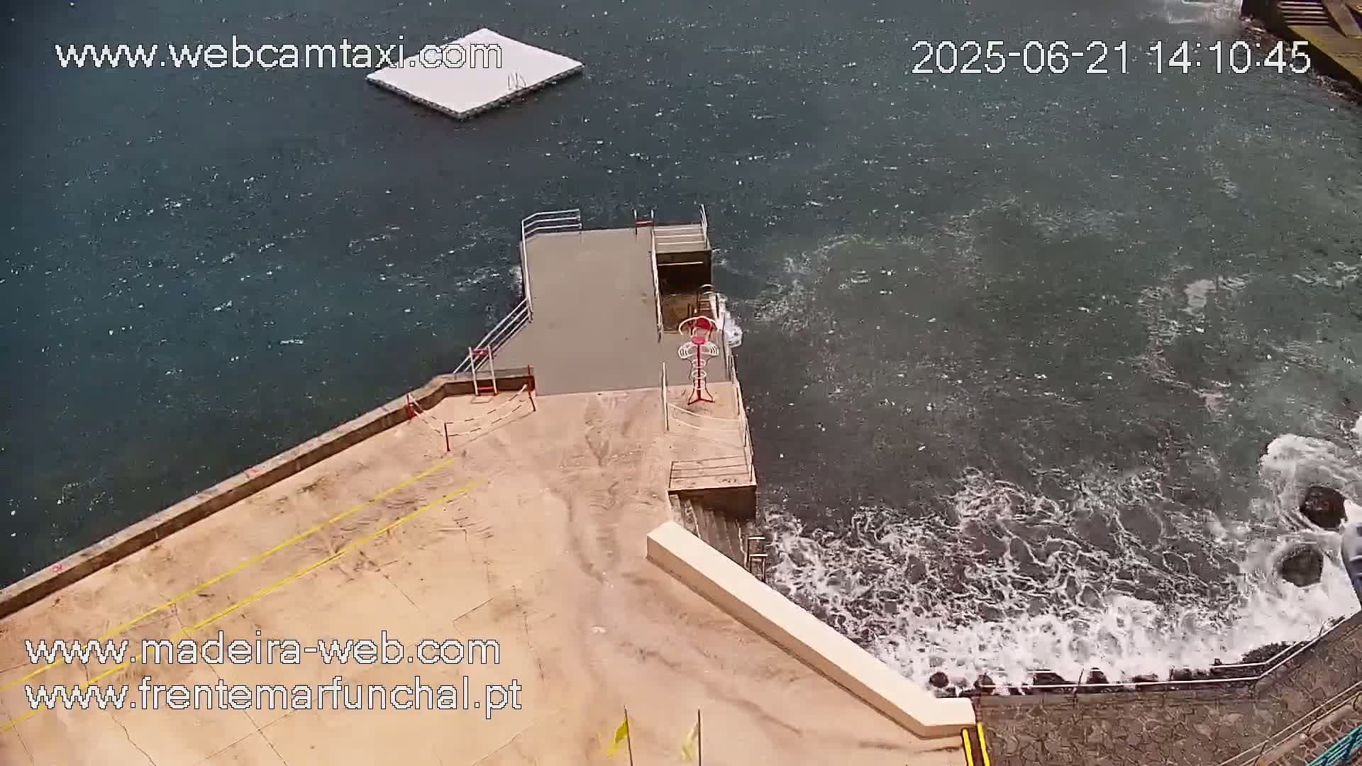 A concrete platform with a lifeguard station overlooks a choppy sea with waves crashing against rocks.