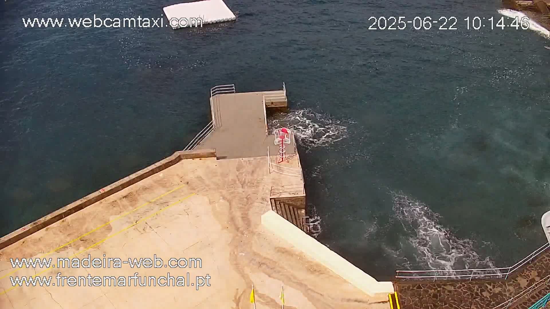 A tan concrete platform with metal railings extends over dark-blue water with small waves.