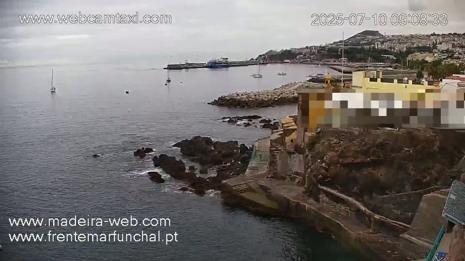 A harbor scene on an overcast day shows a body of water with boats and a rocky shoreline featuring buildings and stairs leading down to the water.