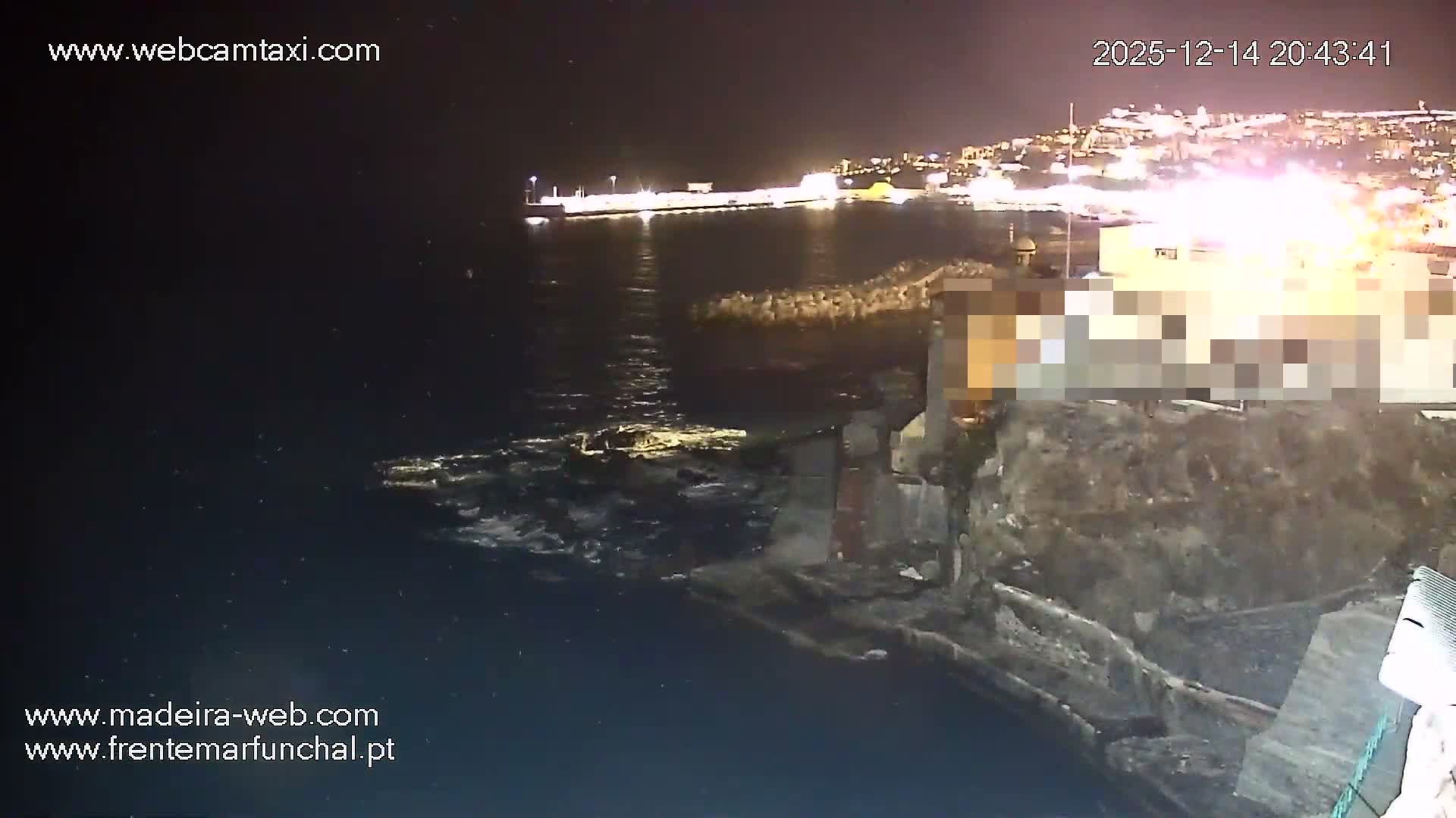 The image displays a dark body of water, likely the sea, reflecting faint lights under a partly cloudy night sky, with a concrete pier and railings visible in the foreground.