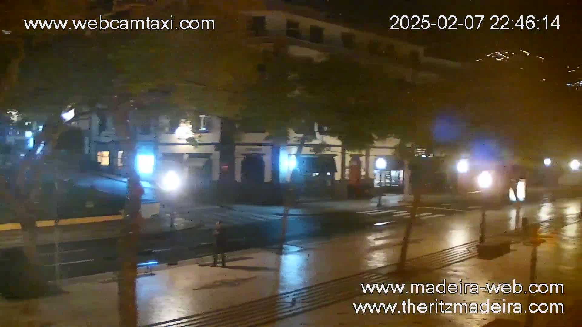 A wet, nighttime street scene shows a row of buildings with streetlights reflecting on the pavement.