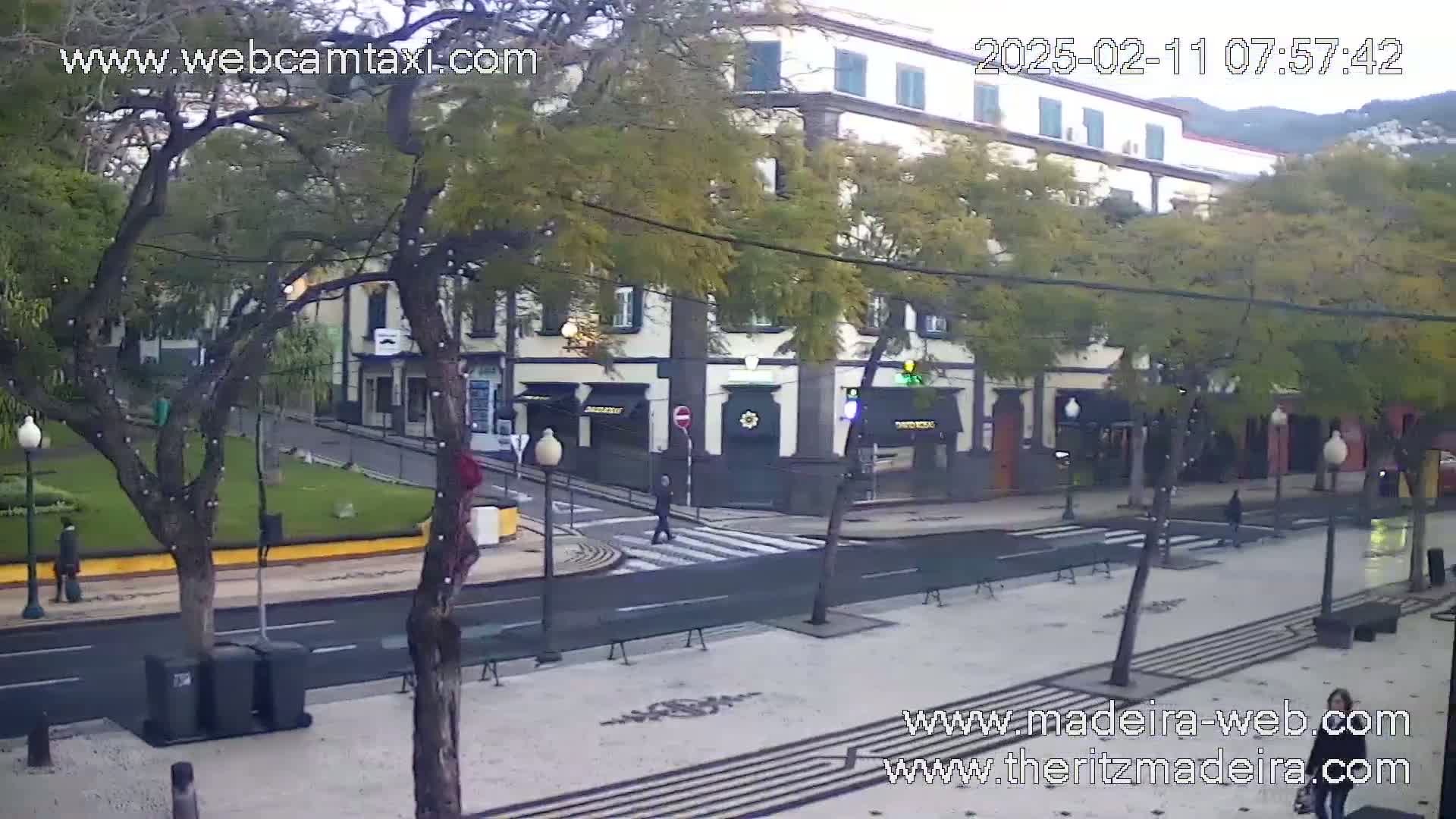 A street scene shows a pedestrian crossing in front of several storefronts on a partly cloudy day.