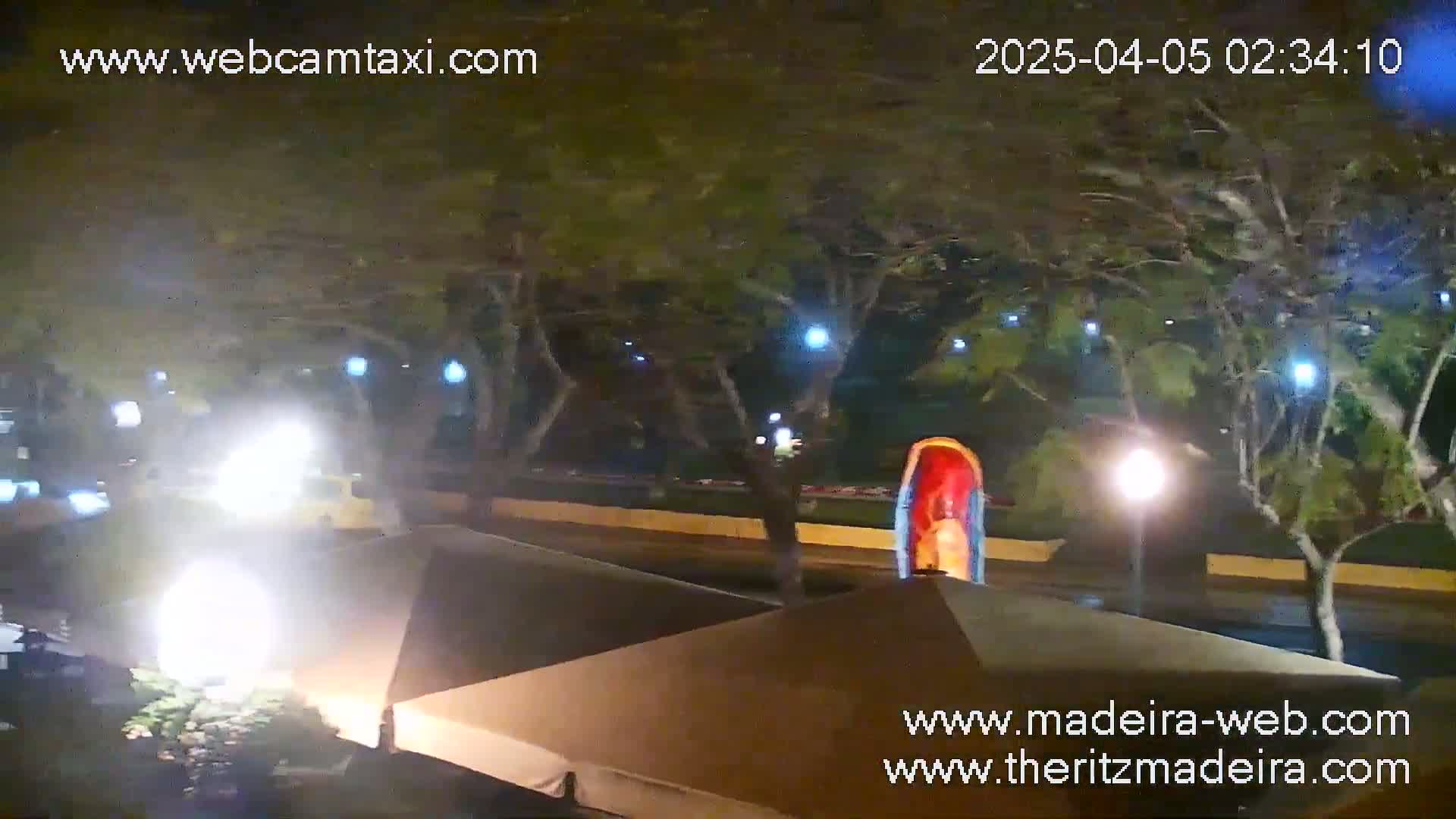 At night, under the cover of trees and streetlights, a partially visible playground structure sits near tan-colored outdoor canopies.